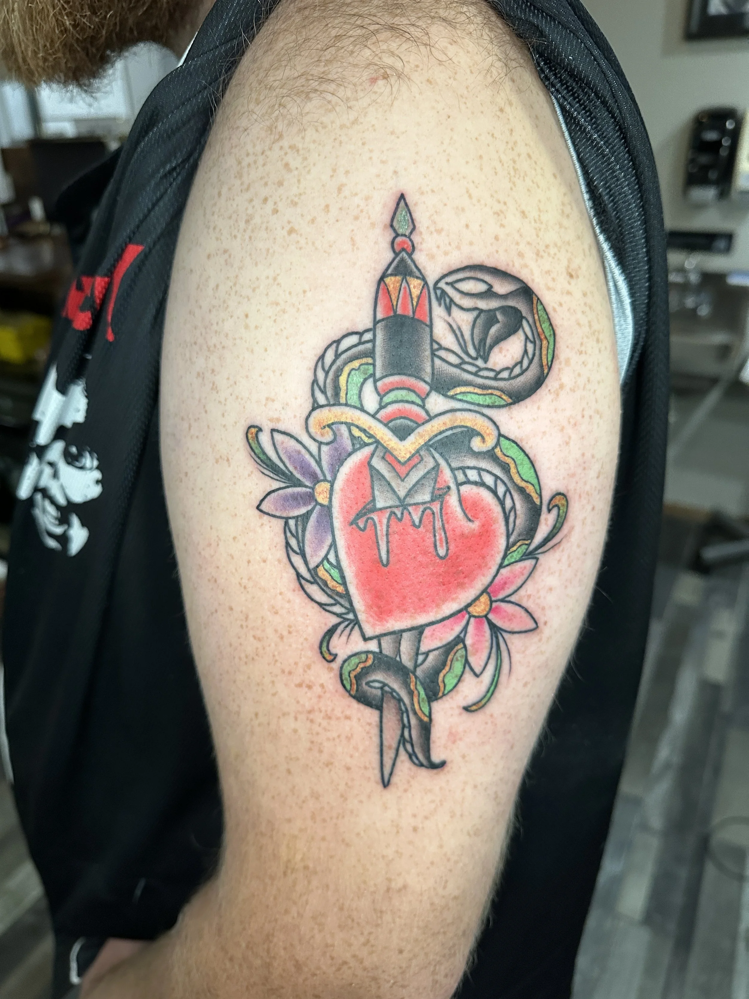 Tattoo of a dagger piercing a heart with flowers, a snake coiled around the dagger, and a dragon head at the top.