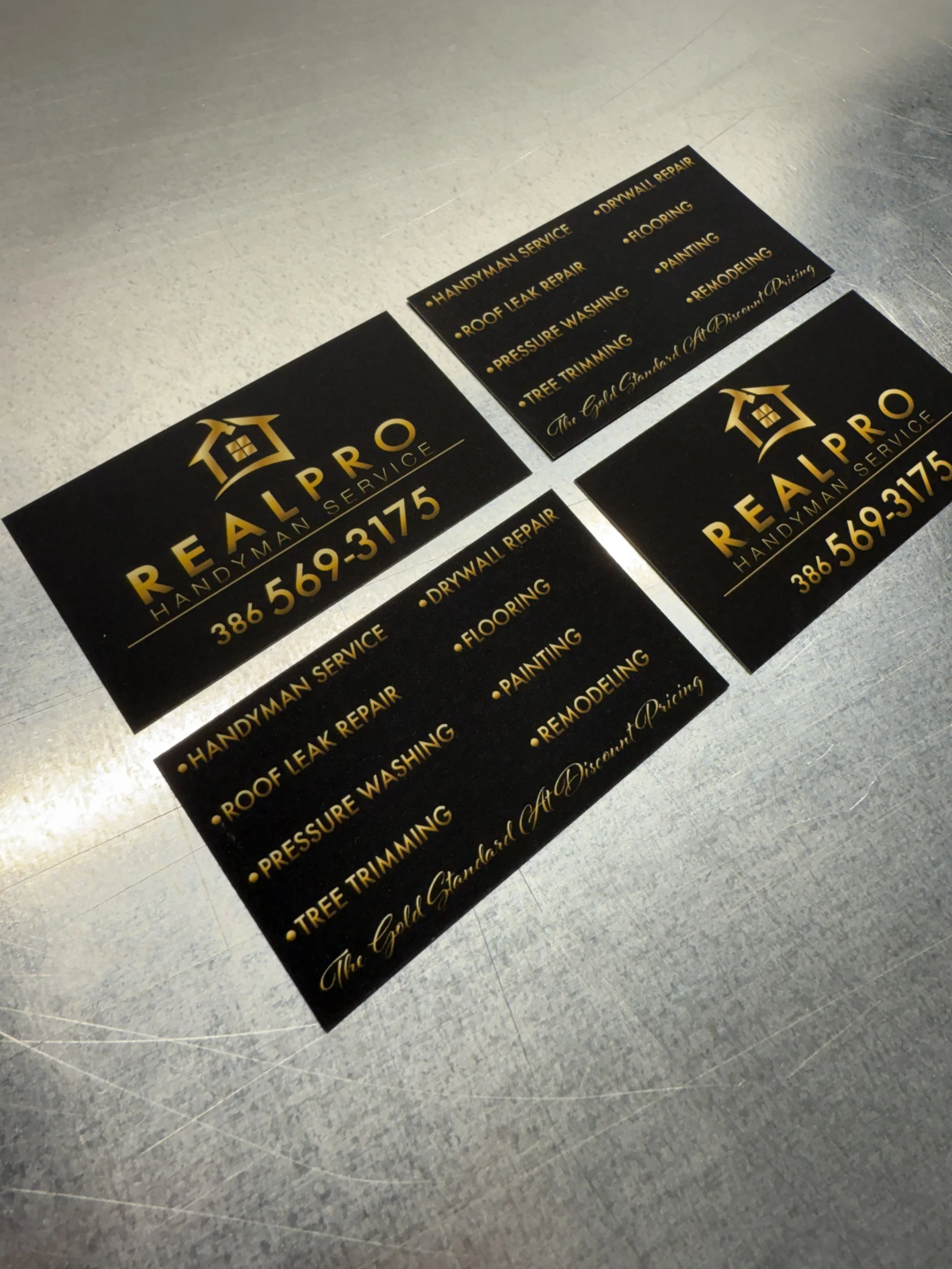 Business cards for RealPro Handyman Service, featuring gold text on a black background, listing services including roof leak repair, pressure washing, tree trimming, drywall repair, flooring, painting, and remodeling, along with contact number 386-56