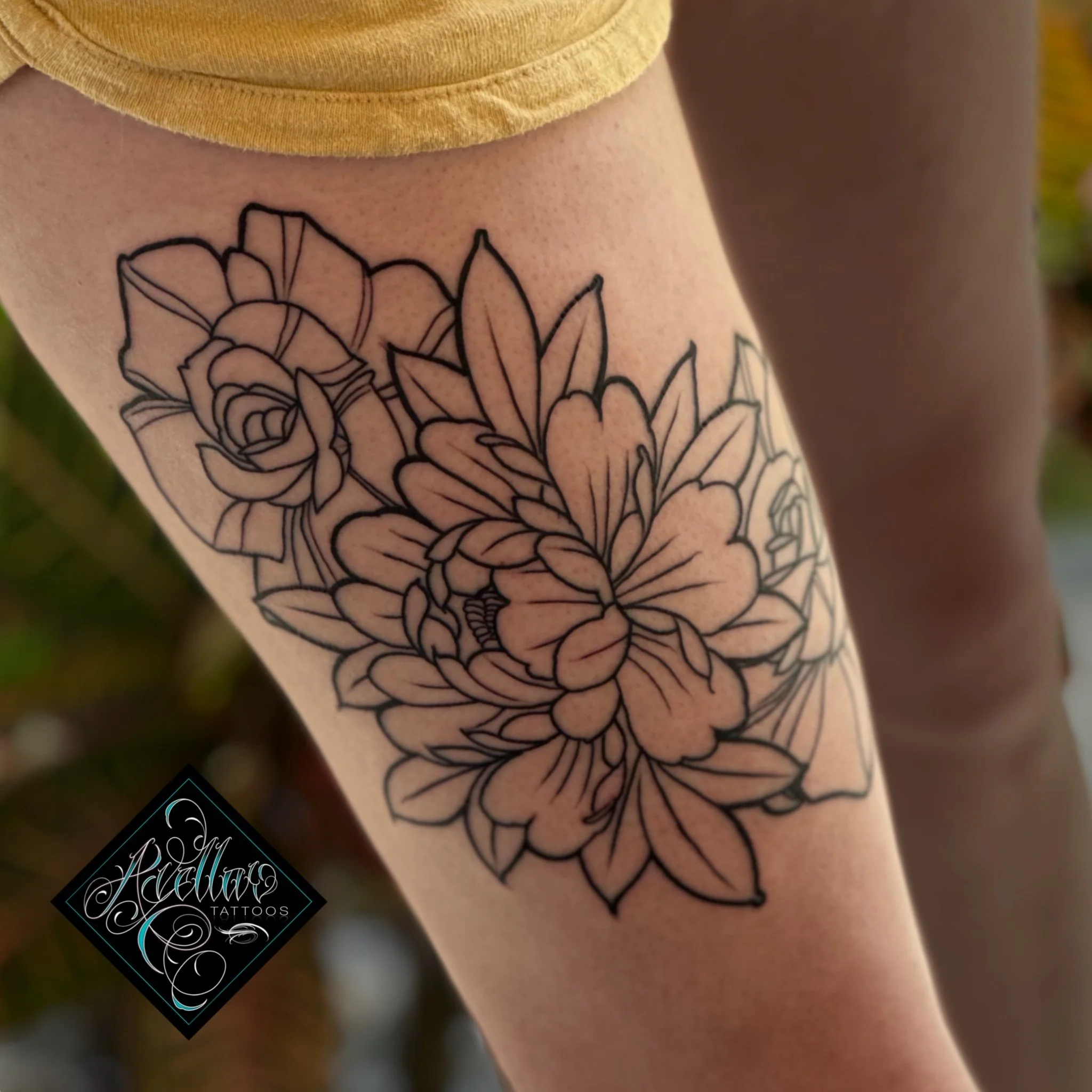 A black outline floral tattoo on a person's leg featuring large flowers and leaves.