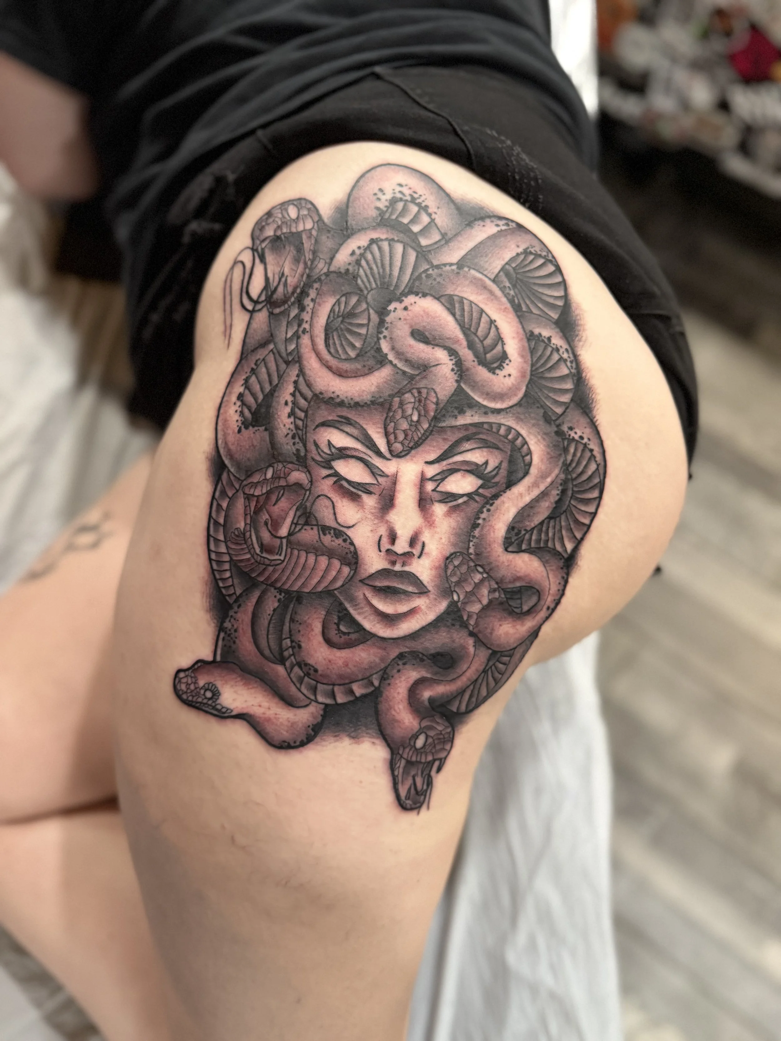 Tattoo of a woman's face with snakes intertwined around her head on a person's thigh.