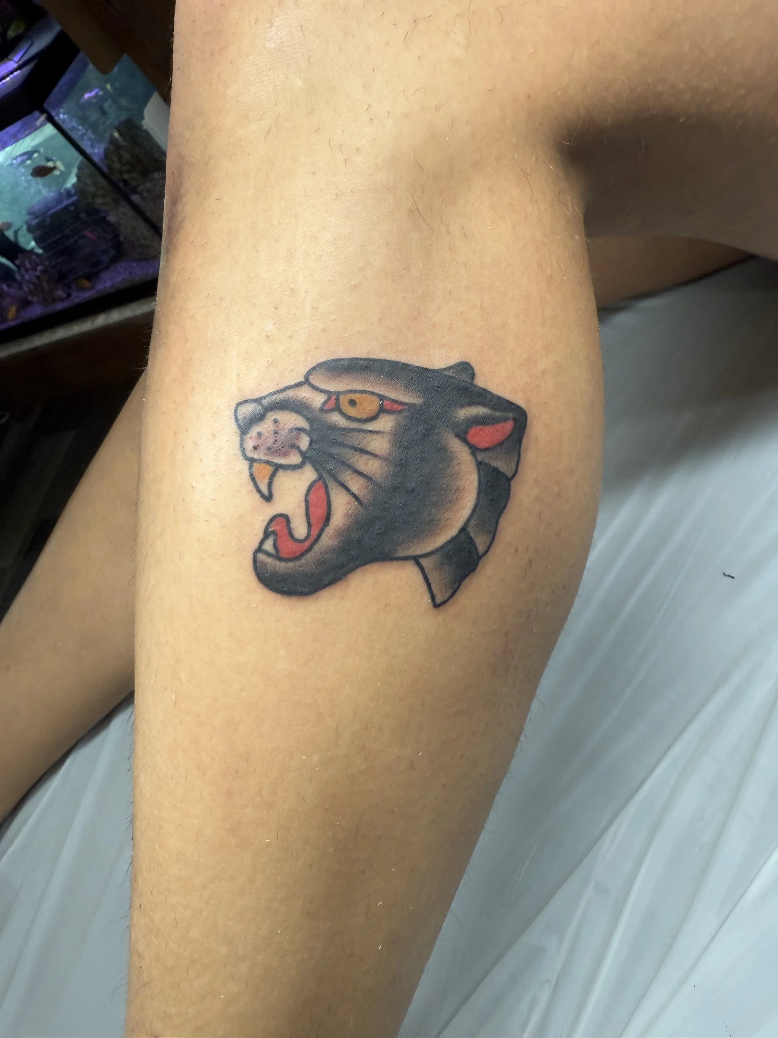 Tattoo of a roaring panther head with black and beige shading, red details in the eyes and inside the mouth.
