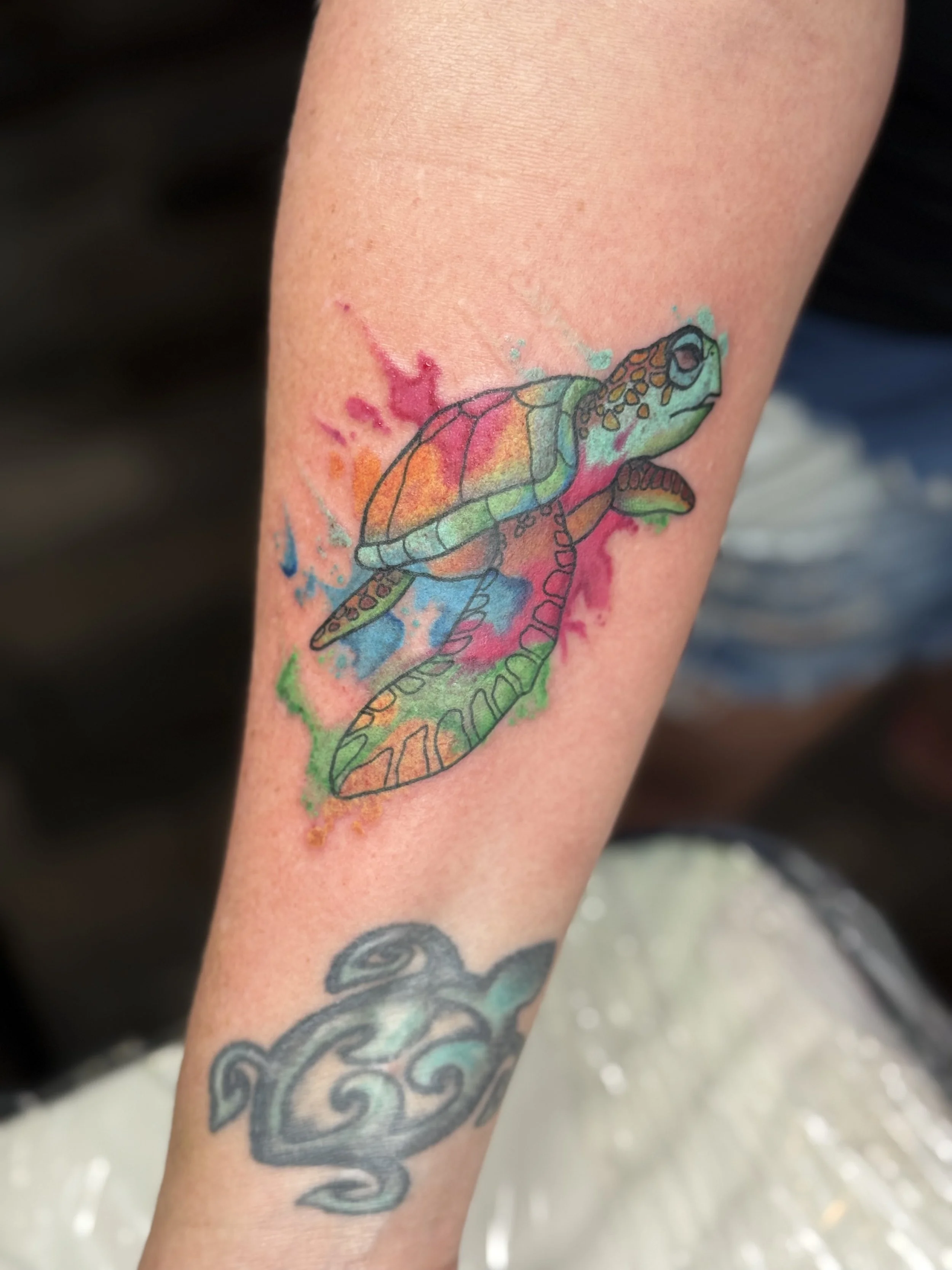 Colorful watercolor style tattoo of a turtle on a person's arm.