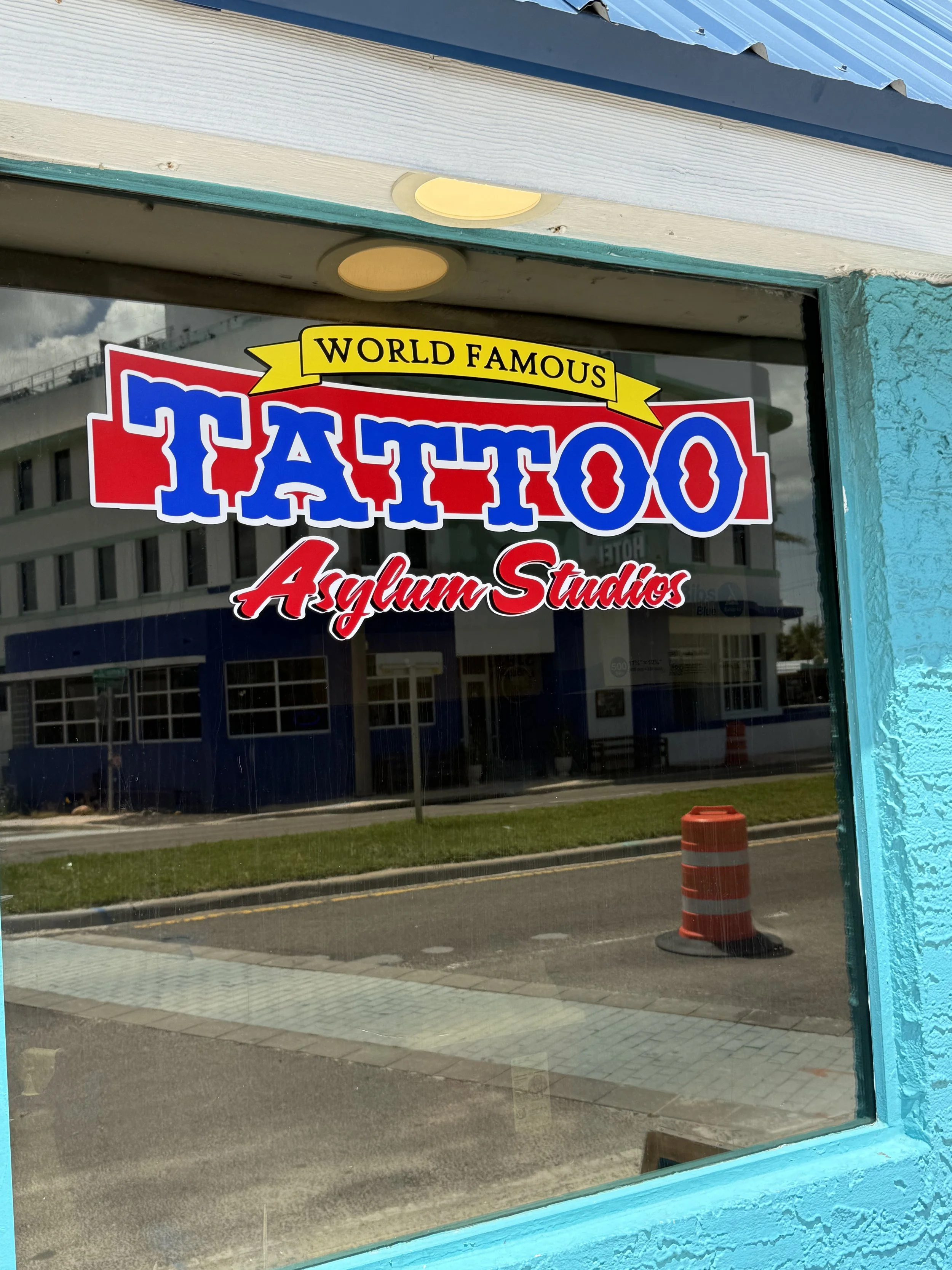 Sign on a window advertising a tattoo parlor called 'World Famous Tattoo Asylum Studios' with colorful text and designs.
