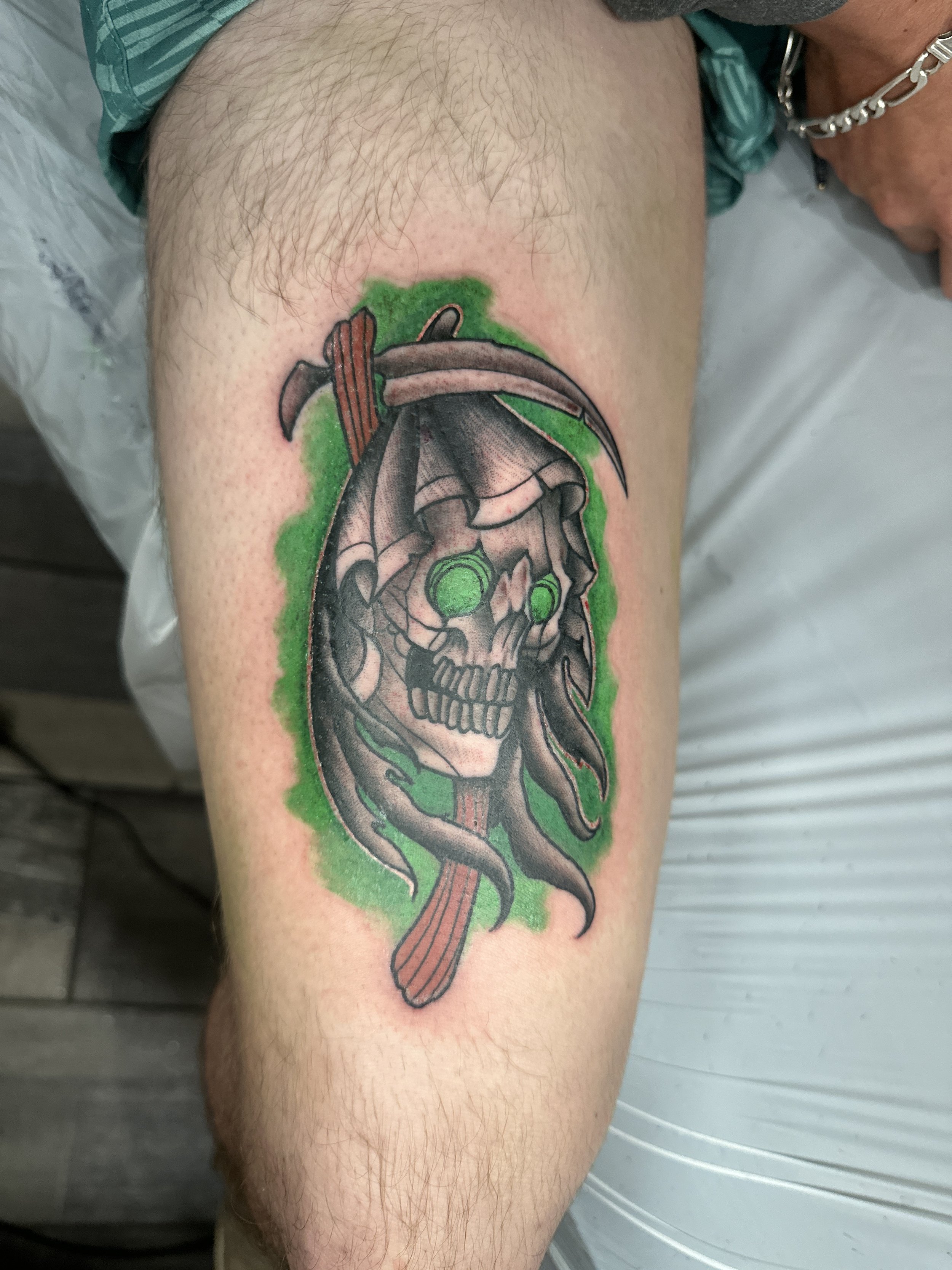 Tattoo of a skull with dreadlocks and a curved sword, surrounded by a green glow.
