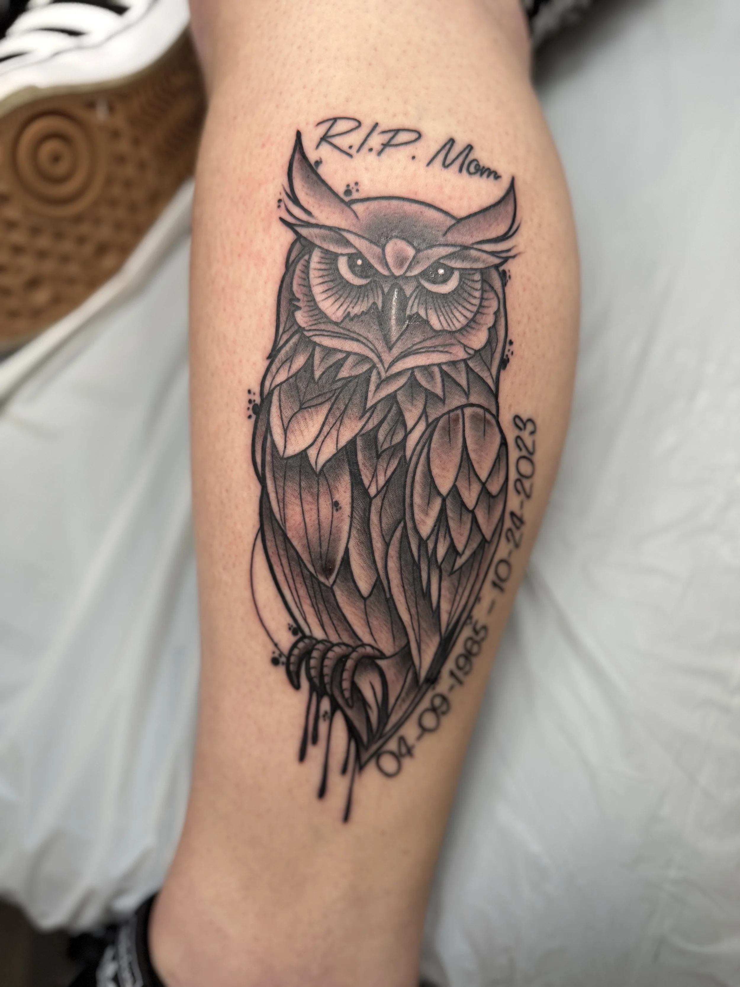 Black and gray tattoo of an owl on a person's forearm with the text 'R.I.P. Mom' above and dates '04.30.1985 - 10.21.2023' below.