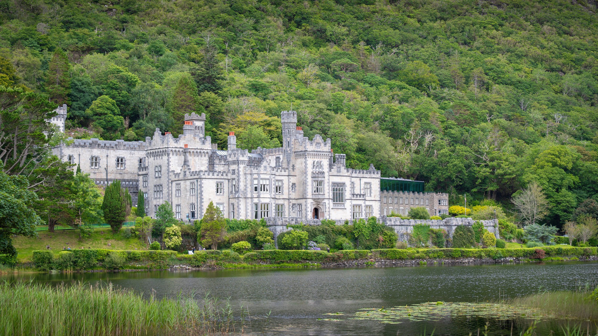 A large white castle with turrets and battlements situated on a lush green hillside near a body of water.