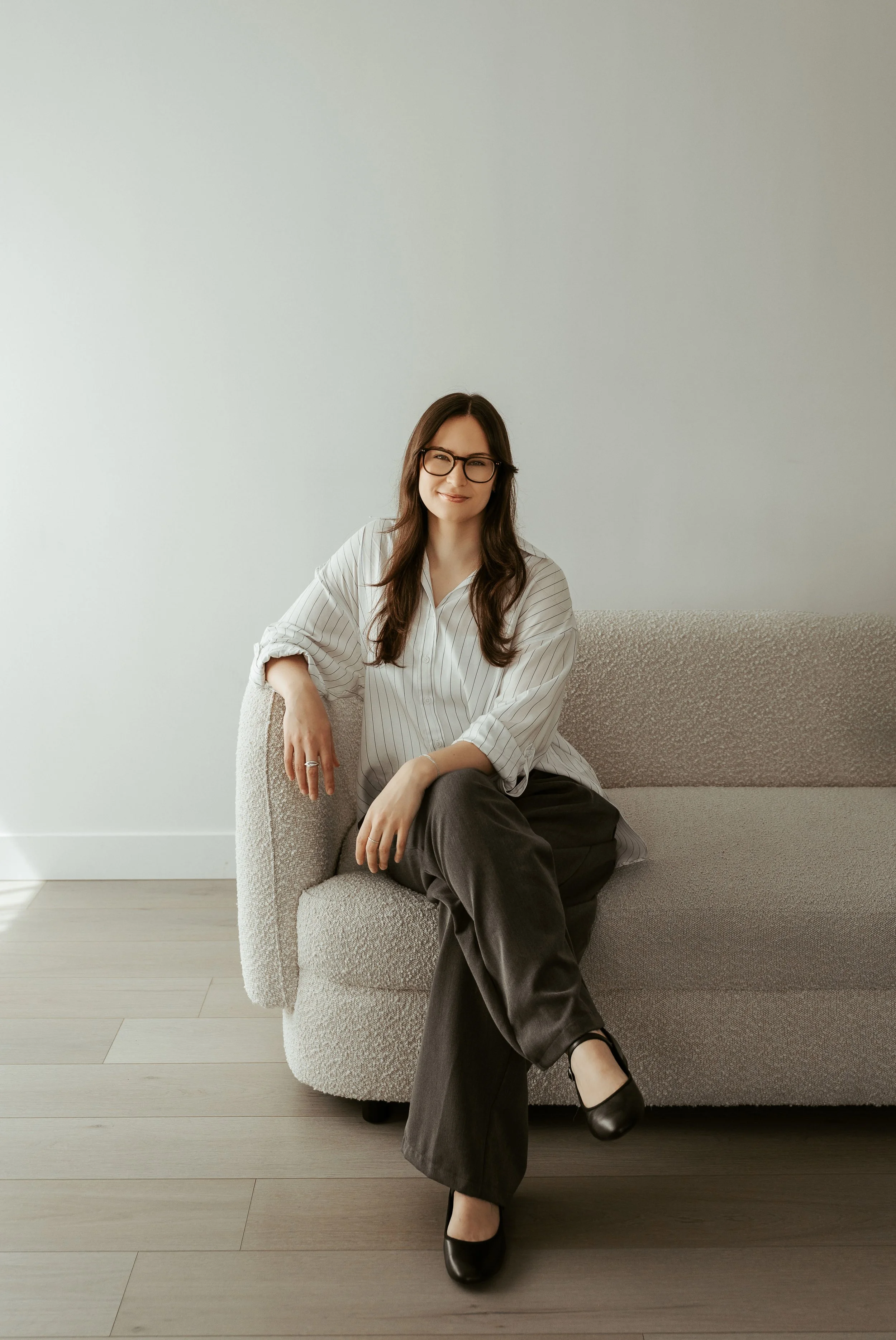 Brown hair counsellor sitting on white sofa looking at the camera. 
