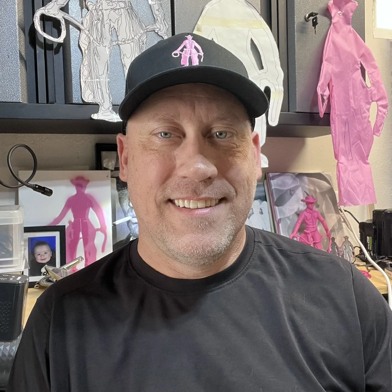A man in an art studio surrounded by pink cowboy artwork in progress.