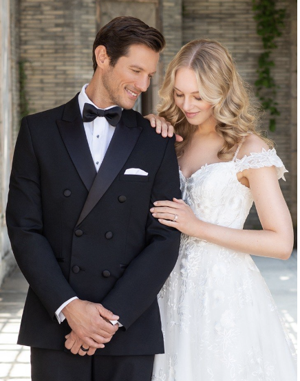 Bride and groom in wedding attire smiling and looking at each other outdoors.