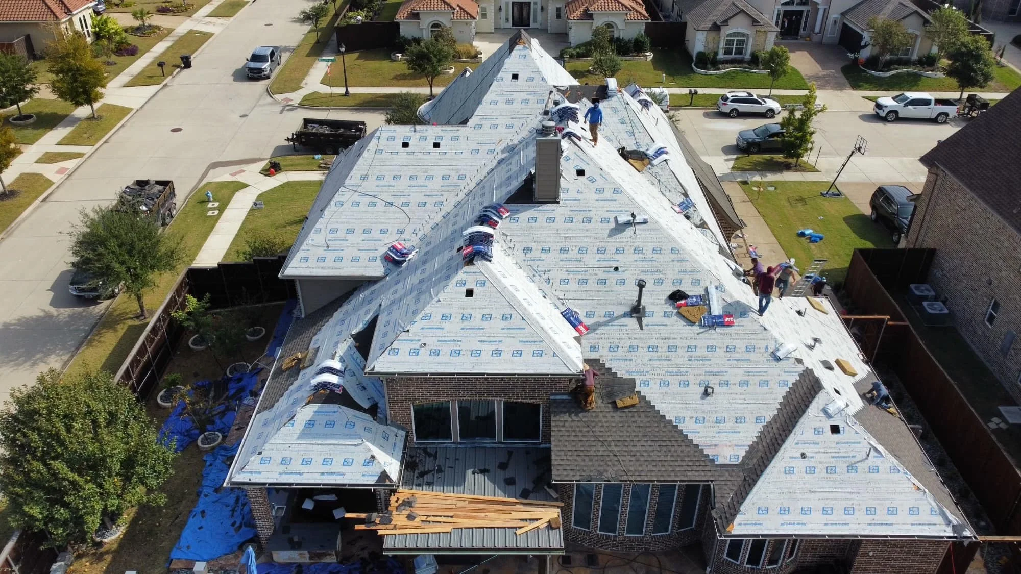 Aerial view of roof replacement in Utah suburb, with contractors installing asphalt shingles on new construction home

