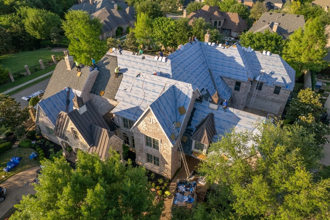 Residential roof installation on large home in Utah, surrounded by trees and neighboring properties — full roof replacement project

