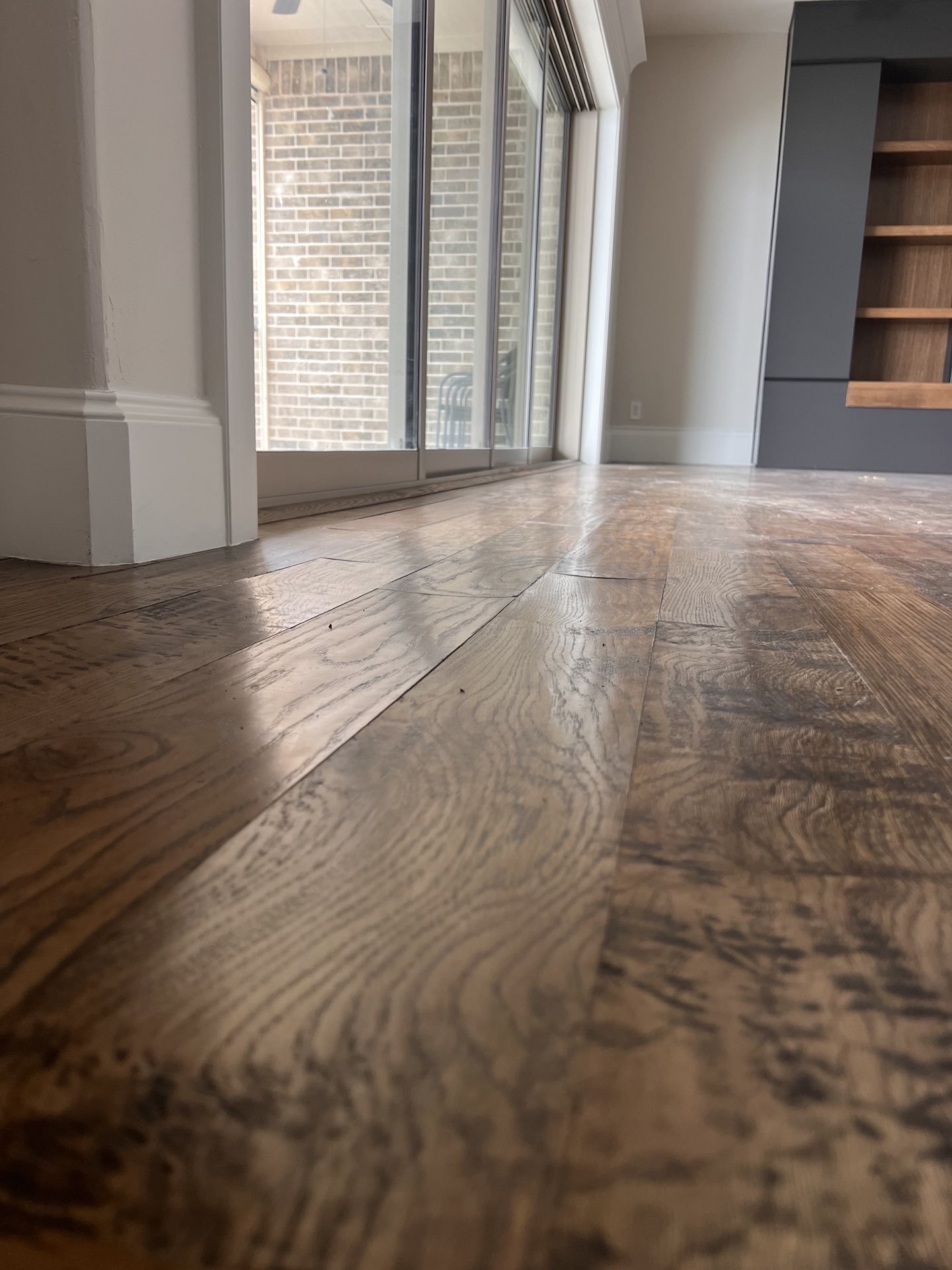 Close-up of wooden floor with sliding glass doors and brick exterior view.