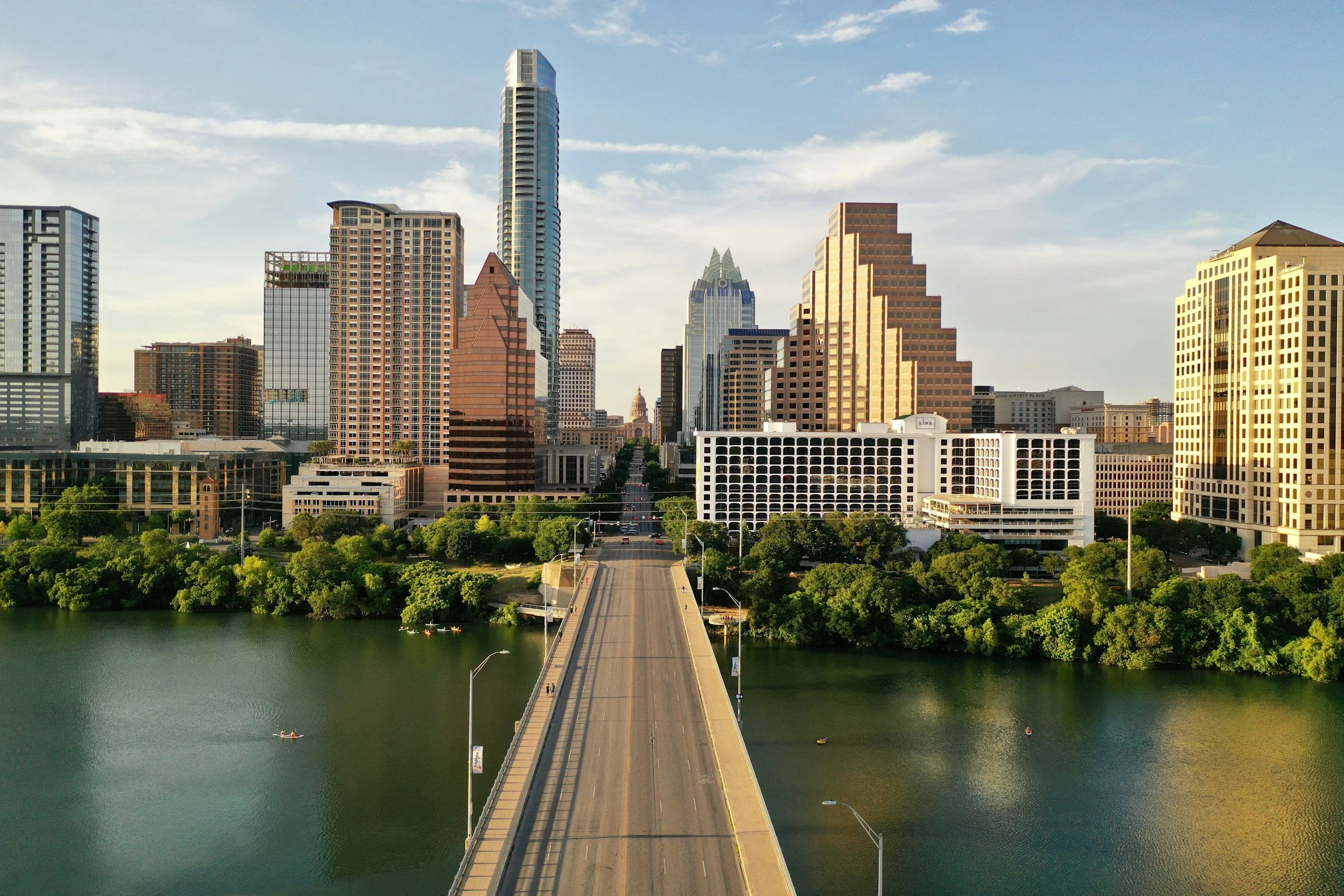 A city skyline with tall modern buildings view from a bridge over a river, in bright daylight.