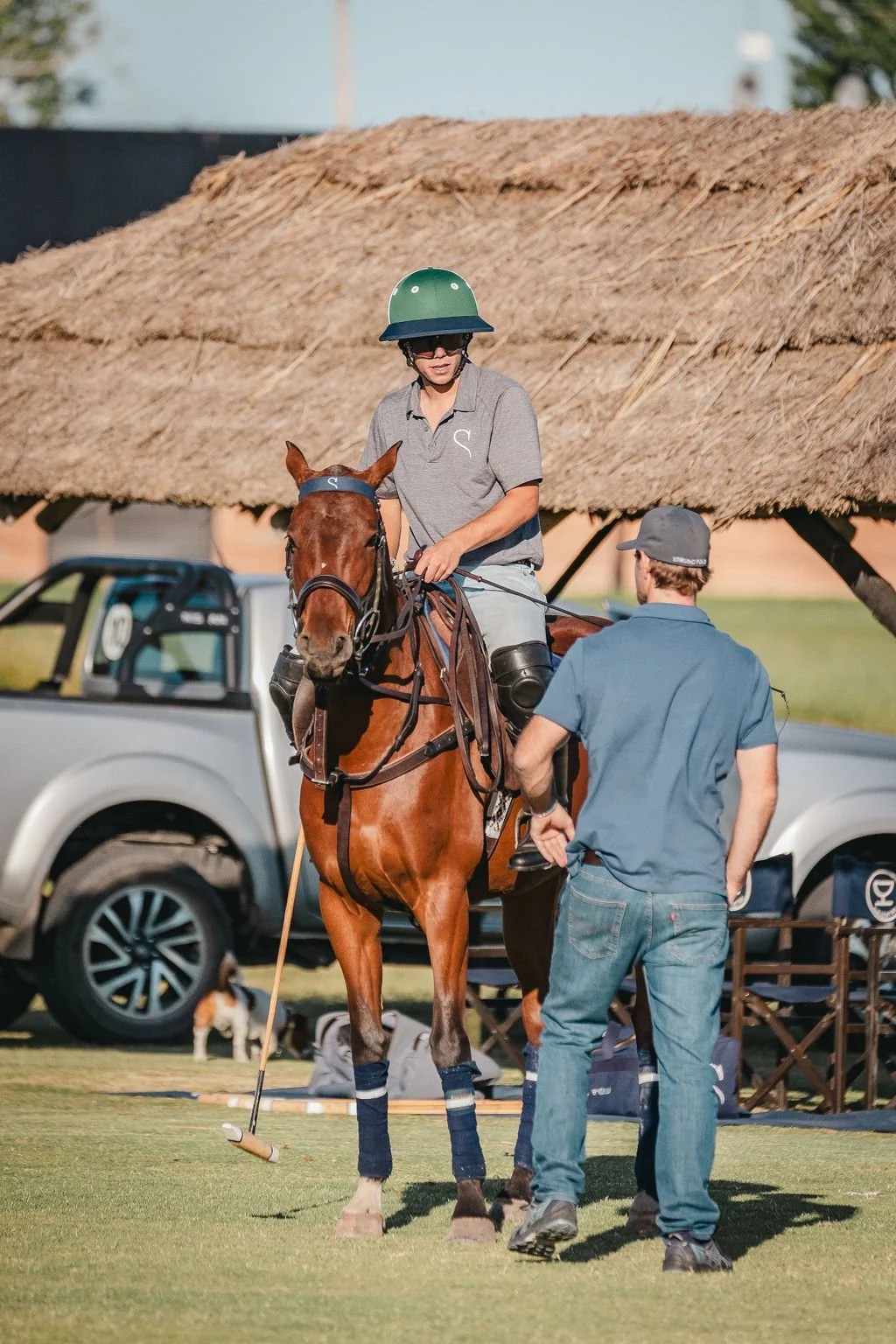 A young person riding a horse playing polo on a grassy field.