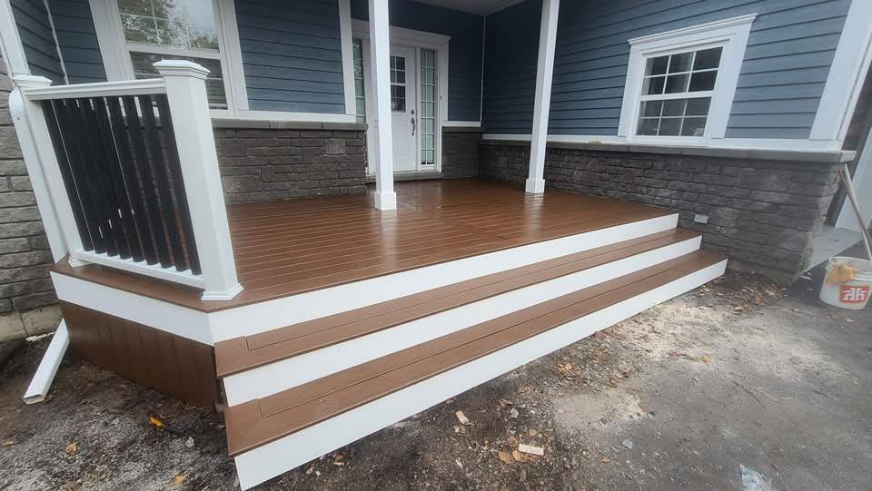Newly installed wooden porch with steps at the back of a house, featuring brown decking, white trim, and black and white railing, with a blue exterior and white window frames.