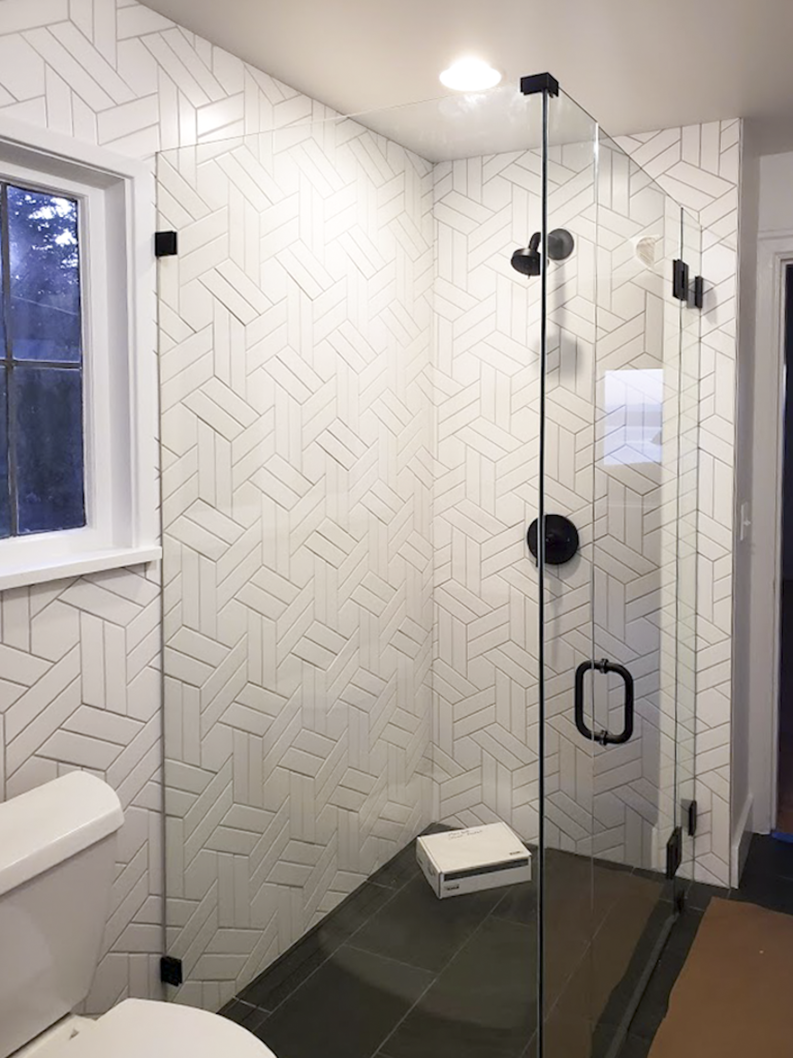 Modern bathroom with geometric tiled walls, a glass shower enclosure with black fixtures, a window, and a white toilet.