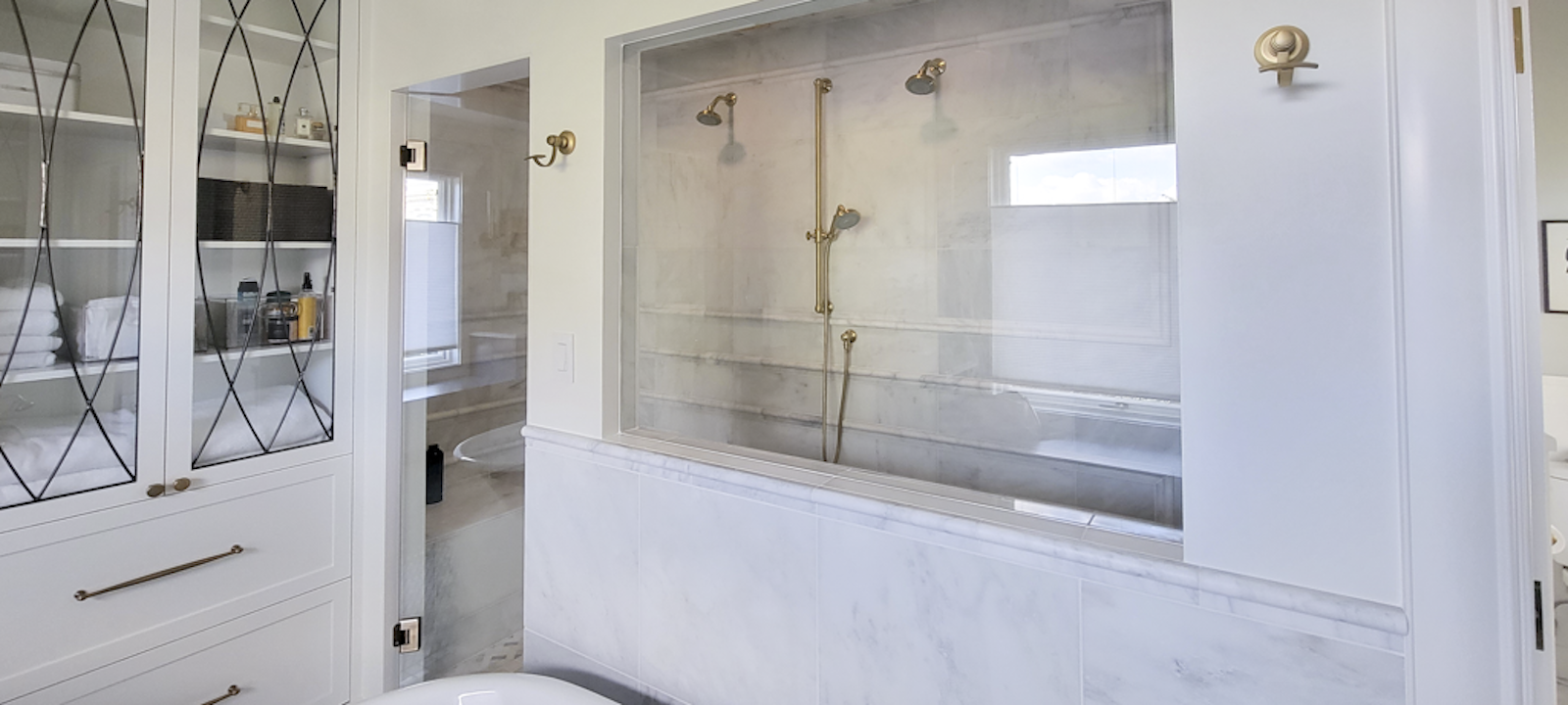 Bathroom with a glass-enclosed shower, gold fixtures, and white cabinetry.