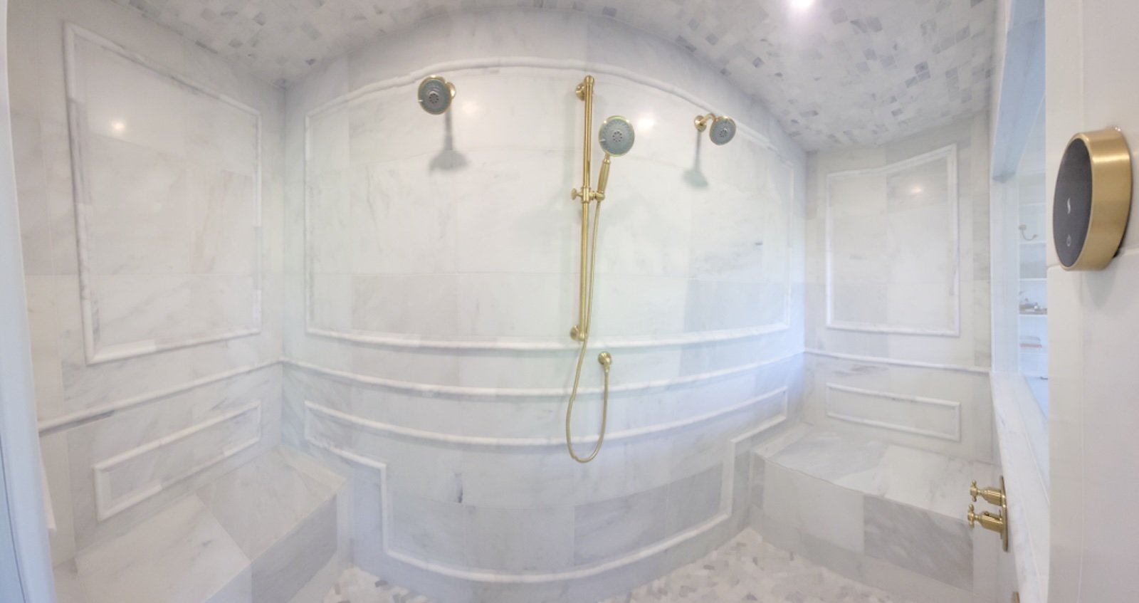 A luxurious shower with marble walls, a gold showerhead, and a built-in marble bench.