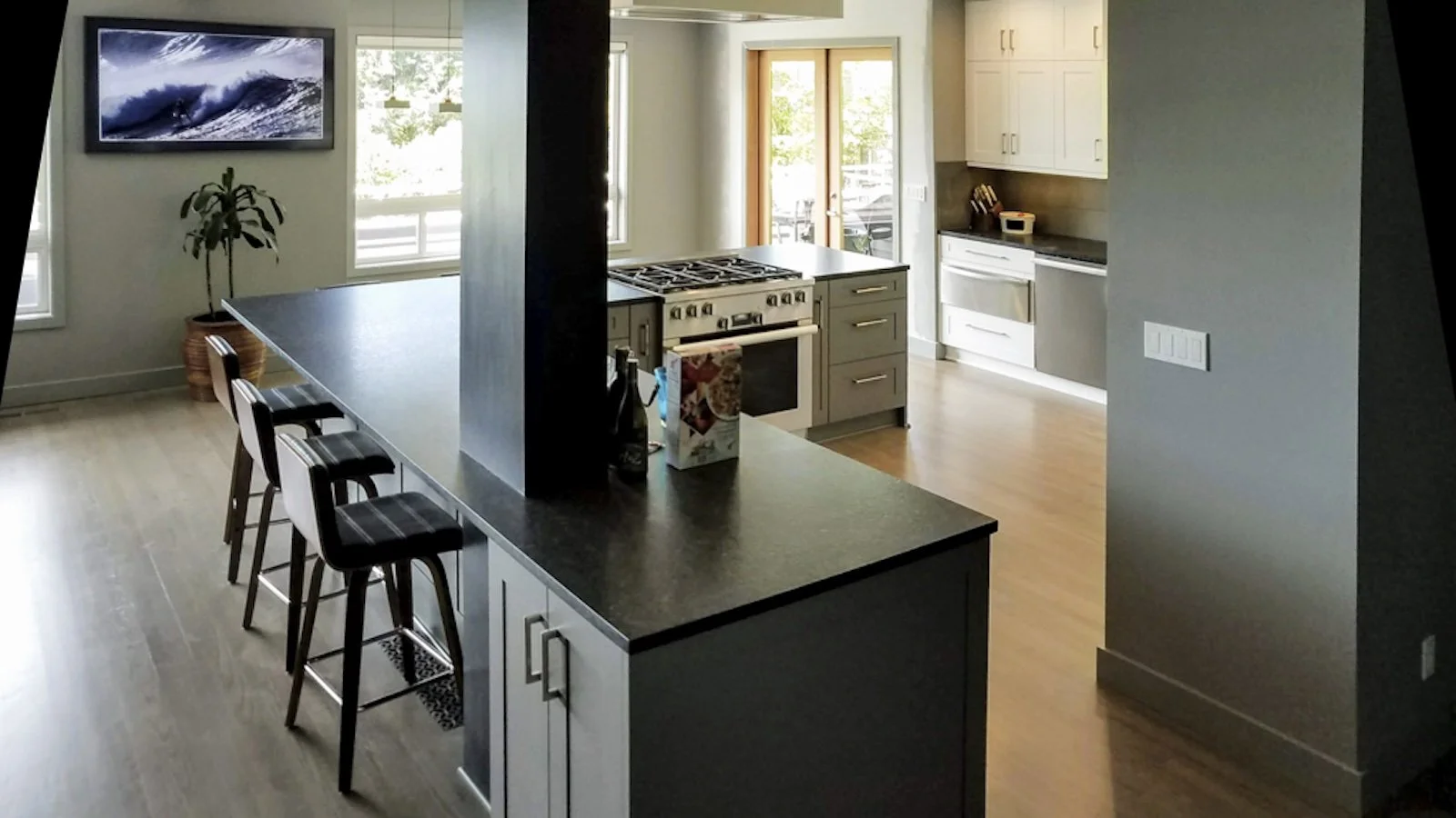 Modern kitchen with a large dark countertop island, white cabinets, a gas stove, and a small dining area with three chairs.