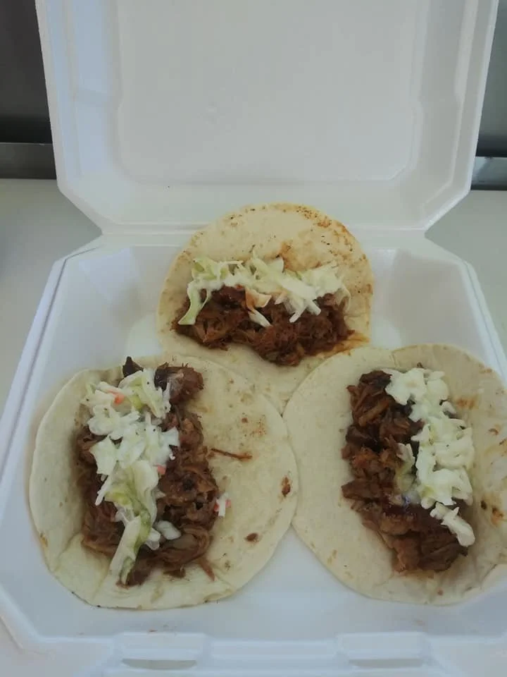 Three tacos filled with shredded beef and lettuce inside a white takeout container.