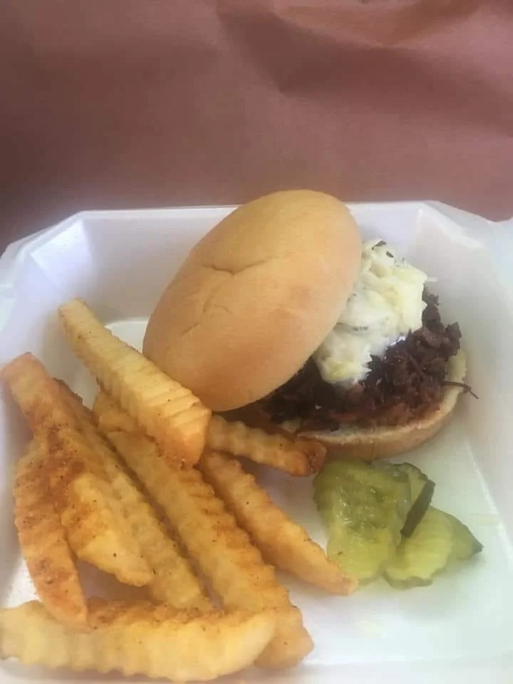 A cheeseburger with potato fries and pickles on a white tray.