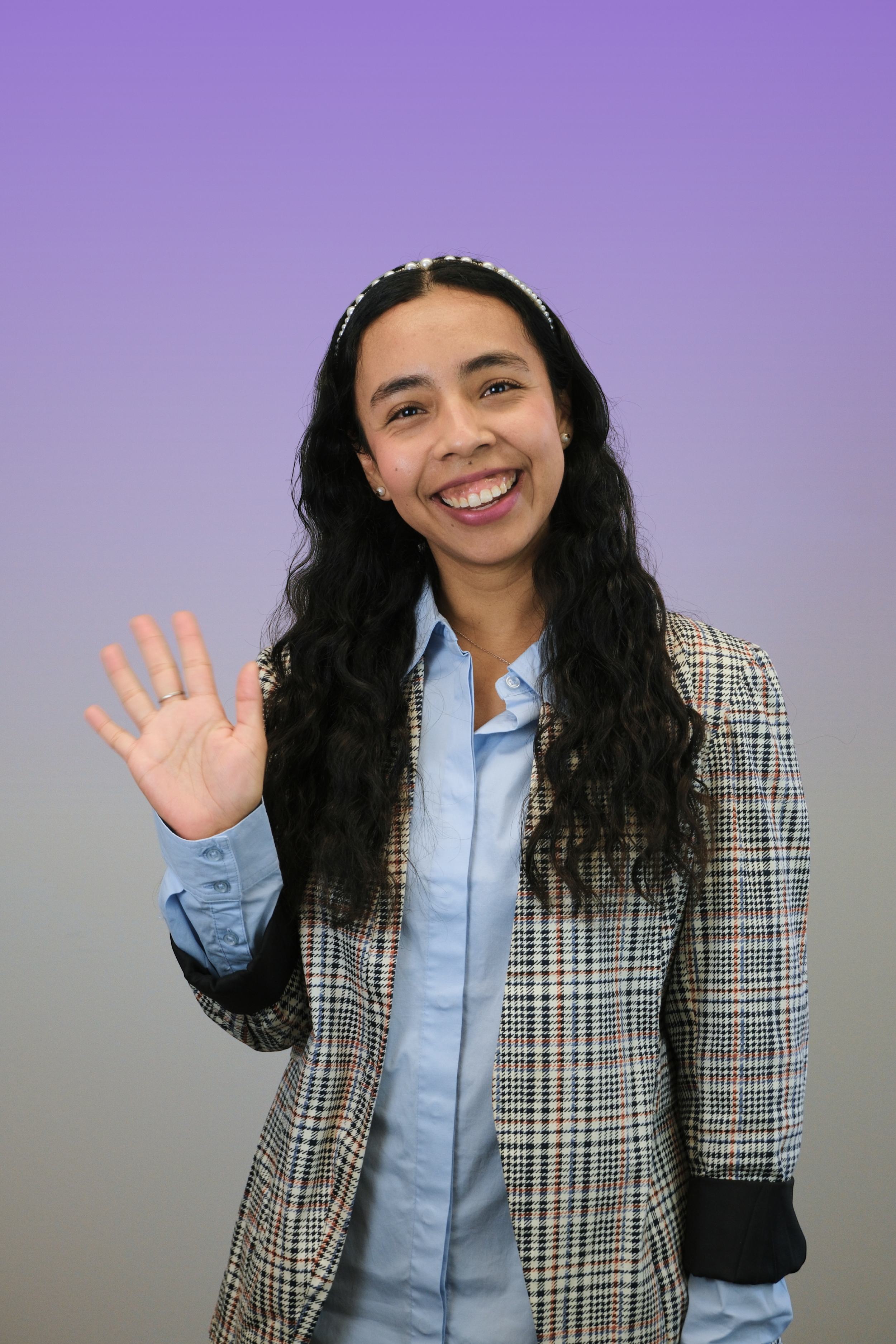 Headshot of a smiling woman with long dark hair, wearing a checkered blazer and white top, against a neutral gray background.