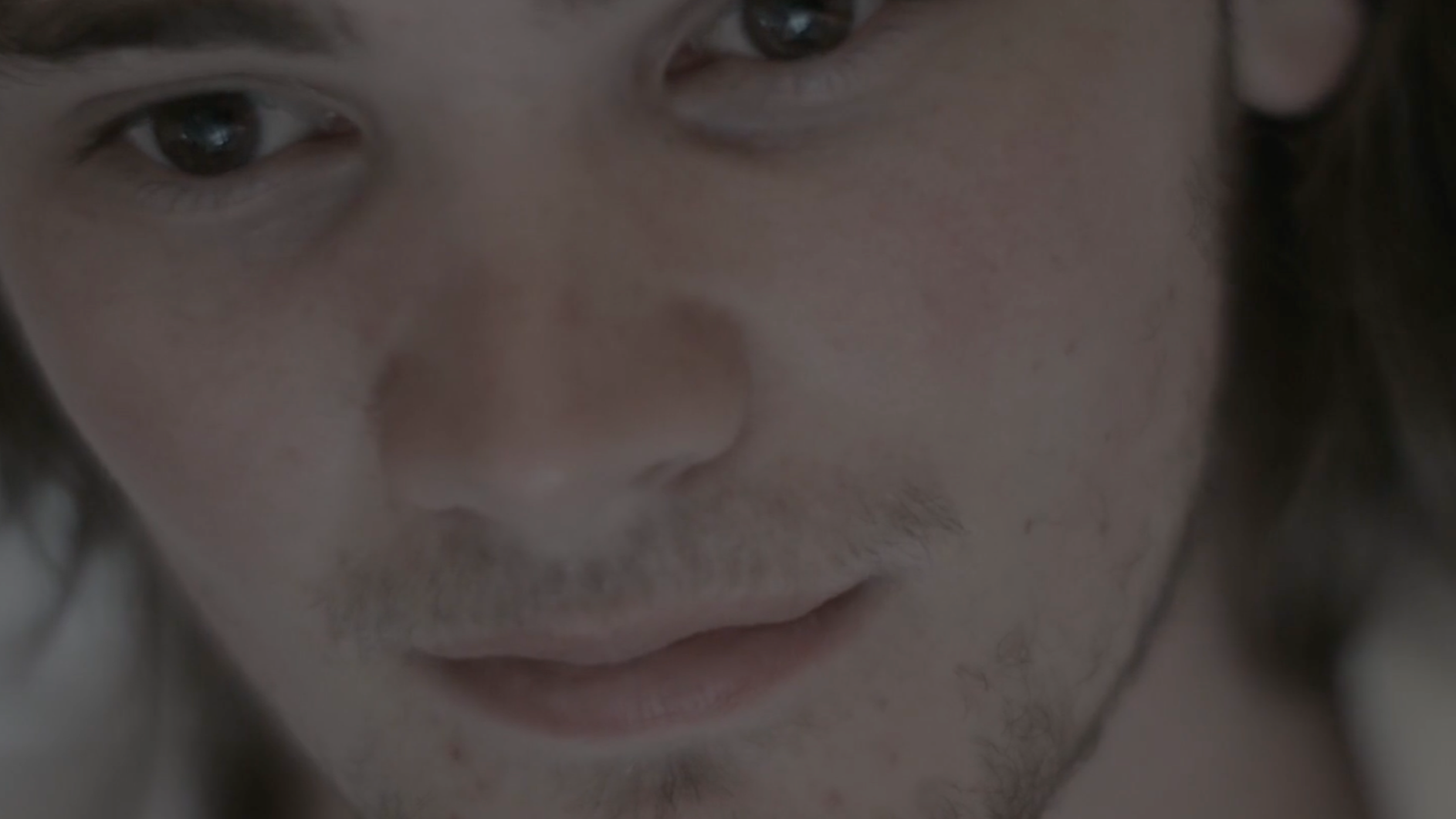 Close-up of a person's face, showing brown eyes, nose, and lips, with some facial hair visible.