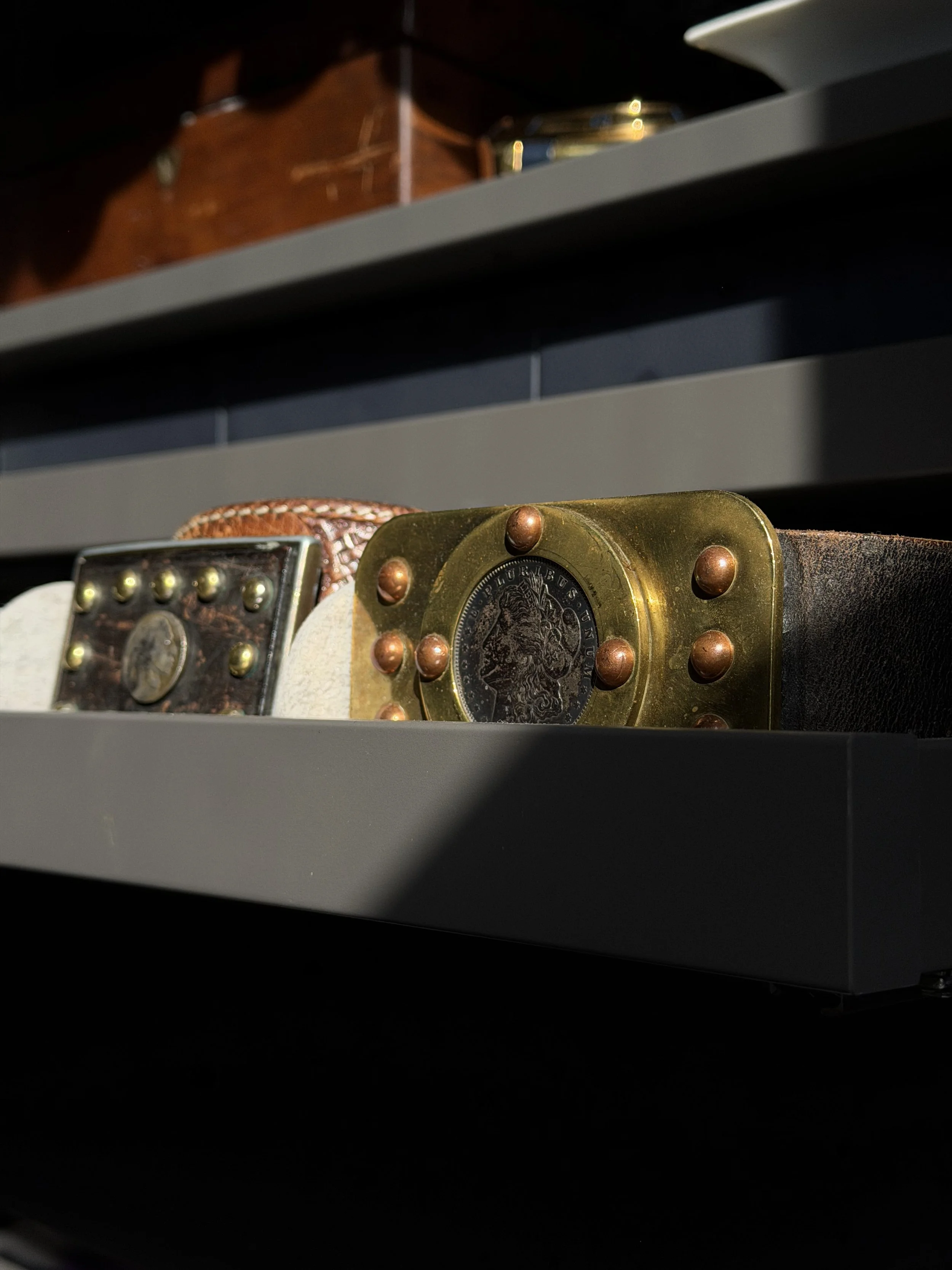 Close-up of a display shelf showing decorative buckle and strap items, with a wooden box and glass jar in the background.