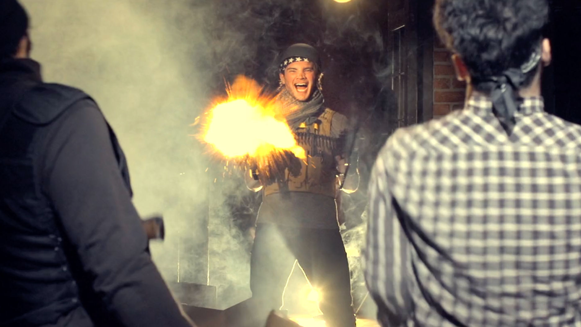 A woman with a bandana on her head and a vest, smiling and holding a sparkler, surrounded by two men in dark jackets, in a dark outdoor setting with brick wall.