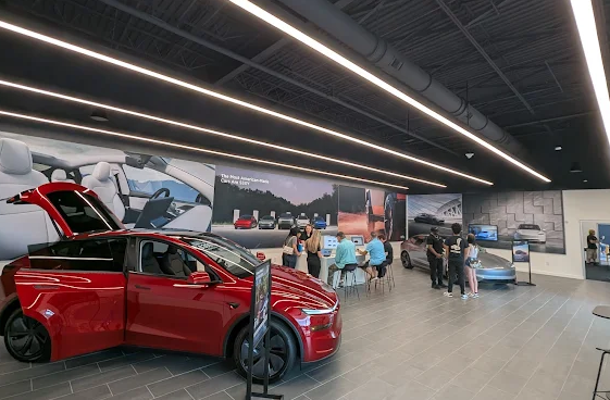 Interior of a Tesla car dealership with a red electric vehicle on display, customers, and sales staff.