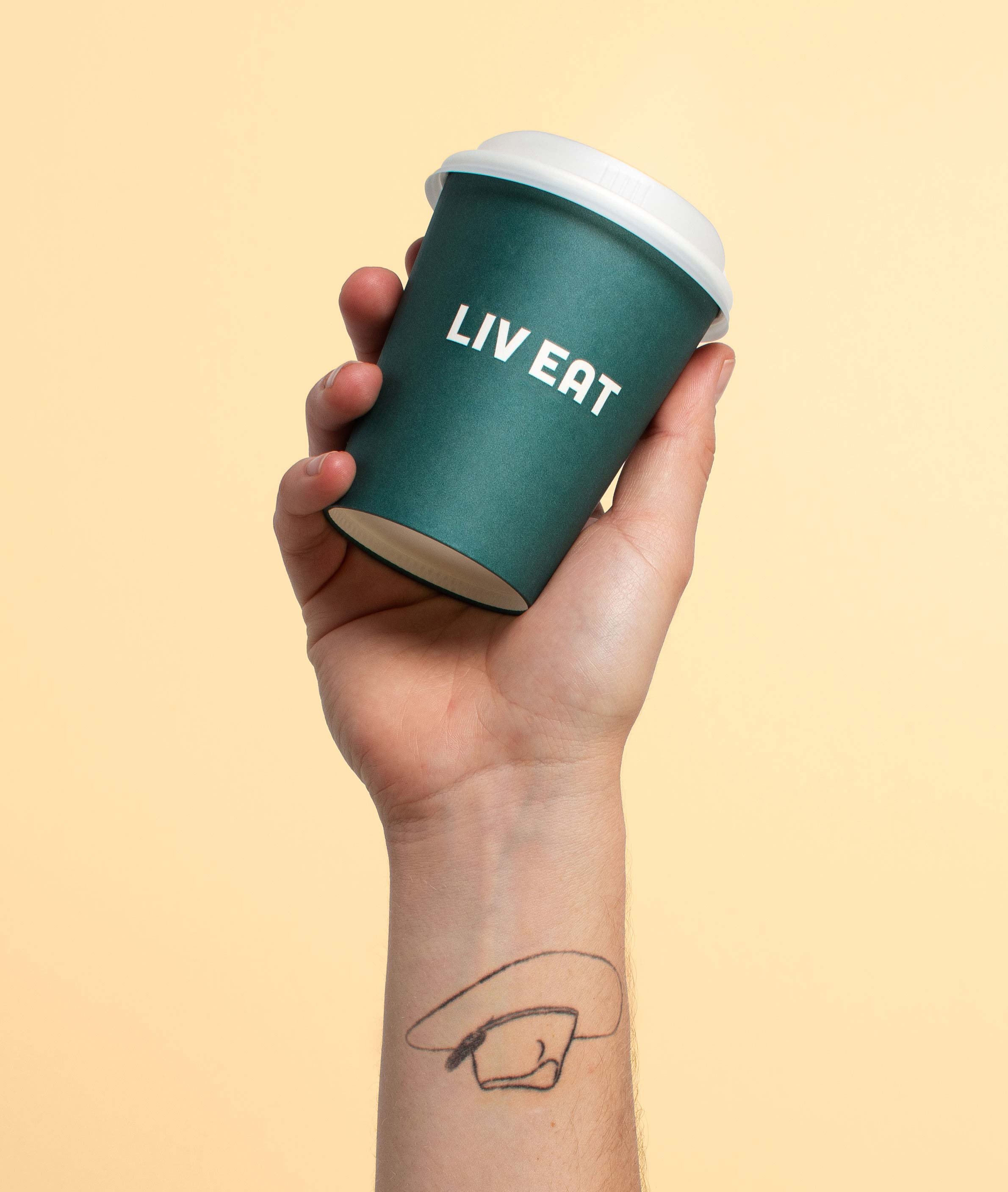 Close-up of a hand holding a teal paper coffee cup with a white lid, with the words "LIVE EAT" printed on it, against a plain light yellow background.