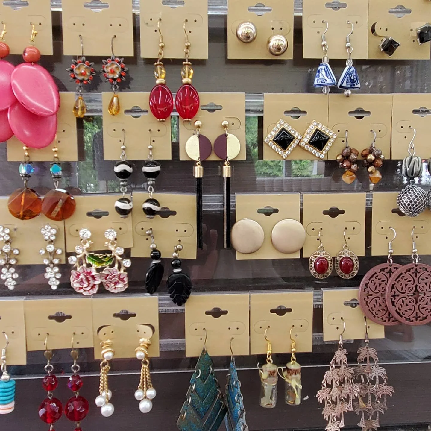 Display of various earrings on a jewelry stand, including floral, geometric, and dangling styles in multiple colors and materials.