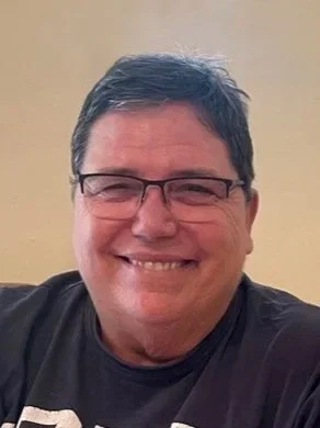 A smiling man with short dark hair, glasses, and a black shirt.