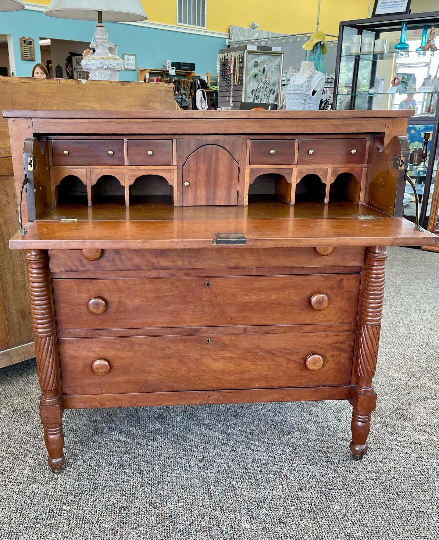 Antique wooden sideboard with drawers and small decorative compartments, set in a thrift store or antique shop.