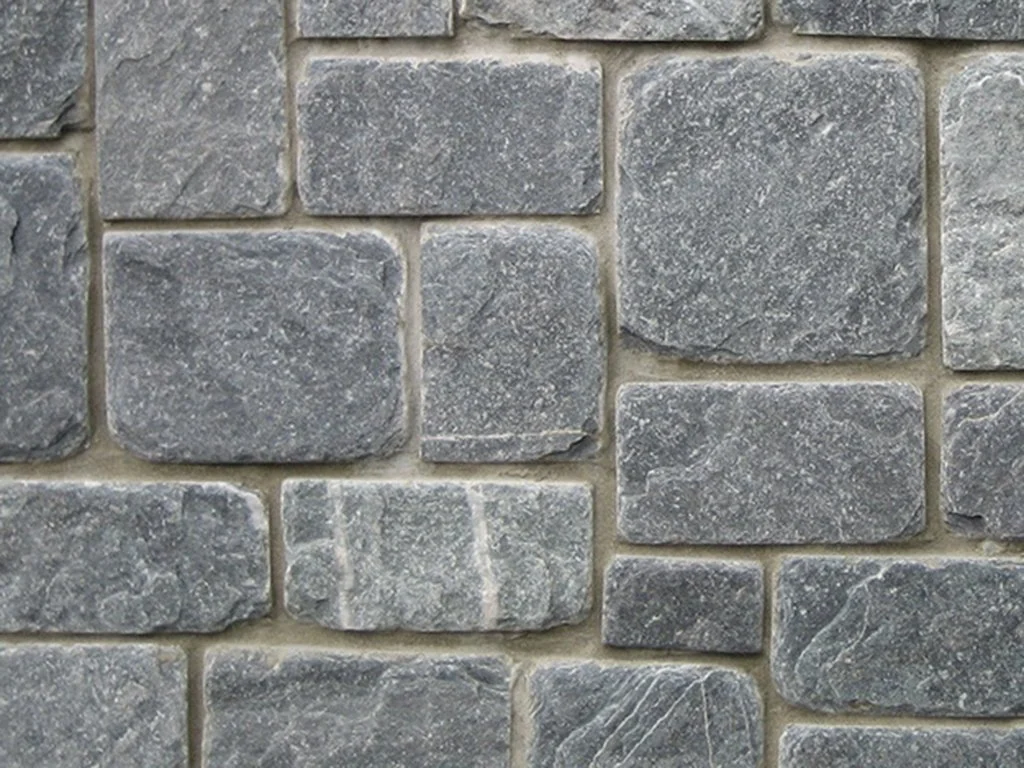 Close-up of a gray stone brick wall with variously shaped rectangular stones.