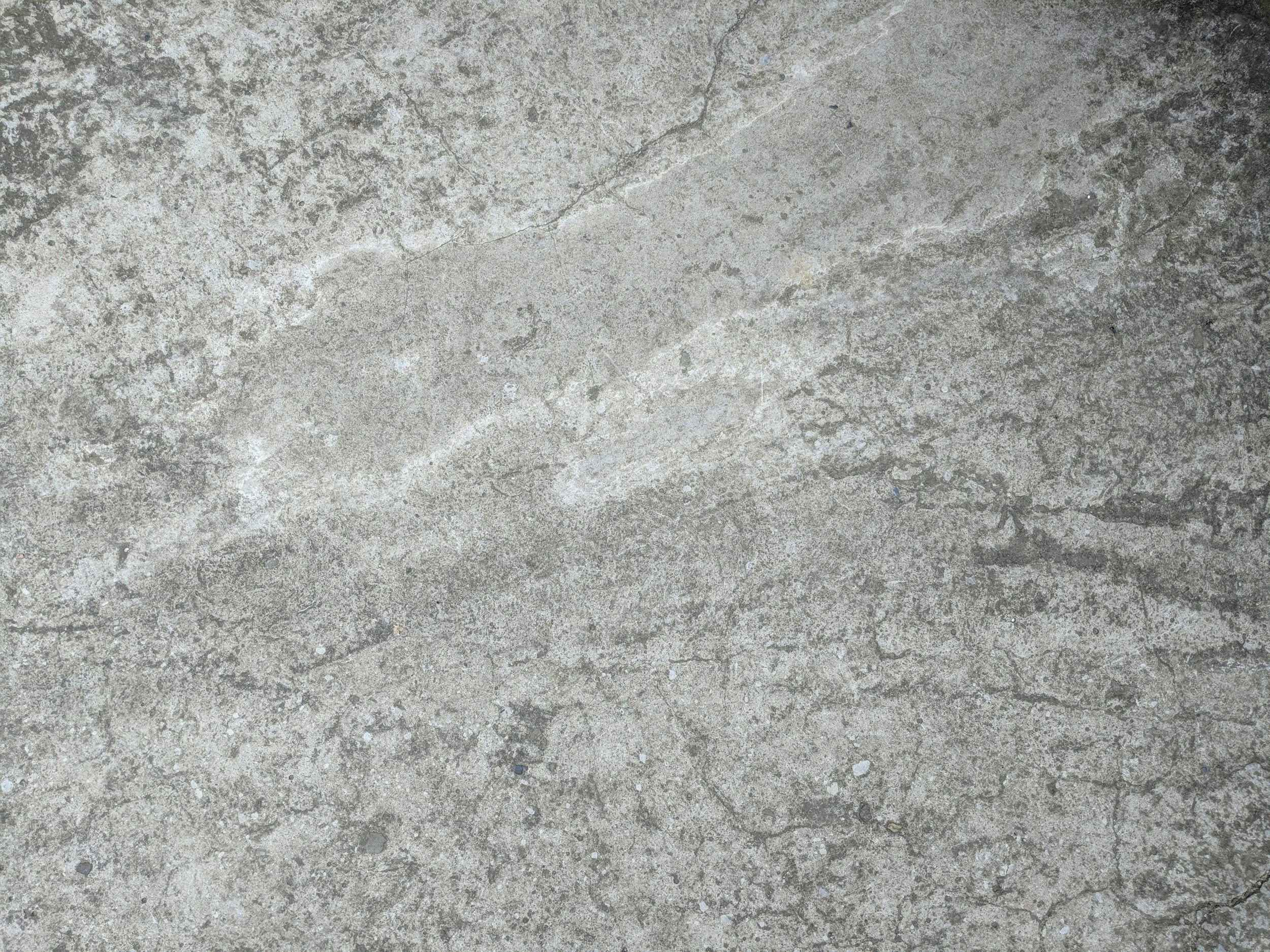A textured concrete surface with various cracks and small pebbles.
