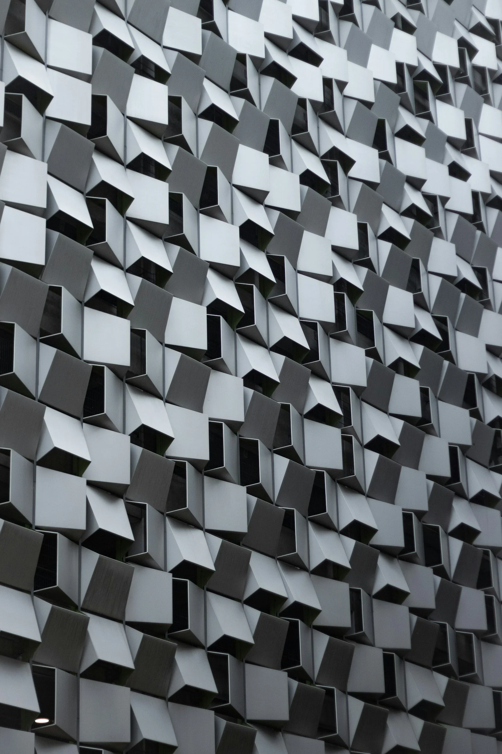 Close-up of a building facade with a pattern of three-dimensional grey and white geometric panels.