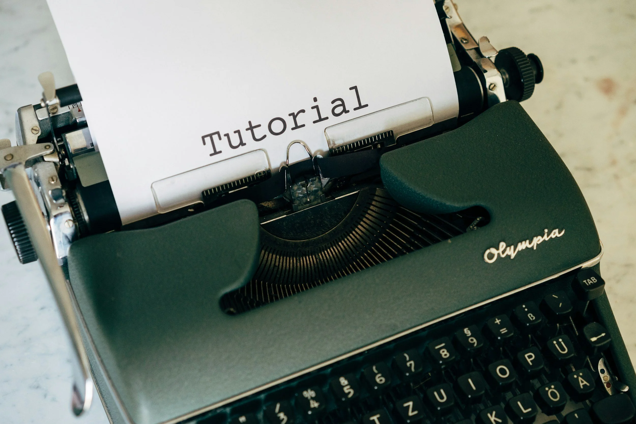 A vintage Olympia typewriter with a sheet of paper labeled 'Tutorial' in uppercase letters.