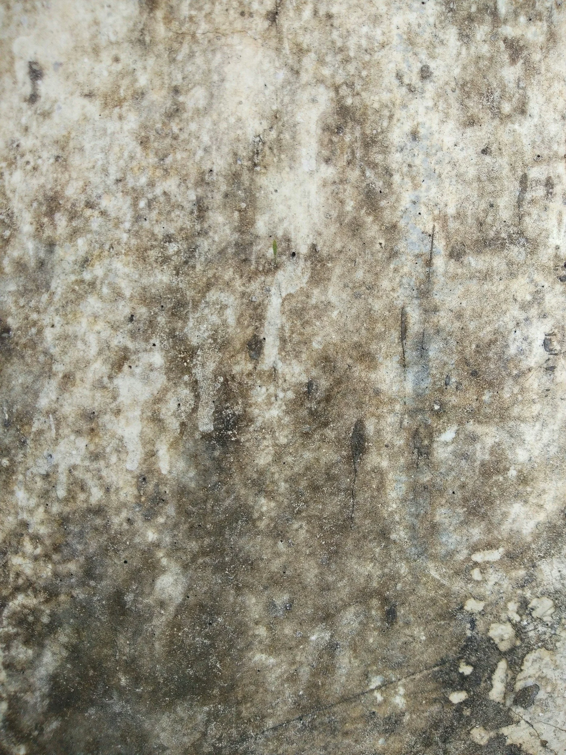 A weathered and stained concrete or stone surface with various marks, discolorations, and small chips.