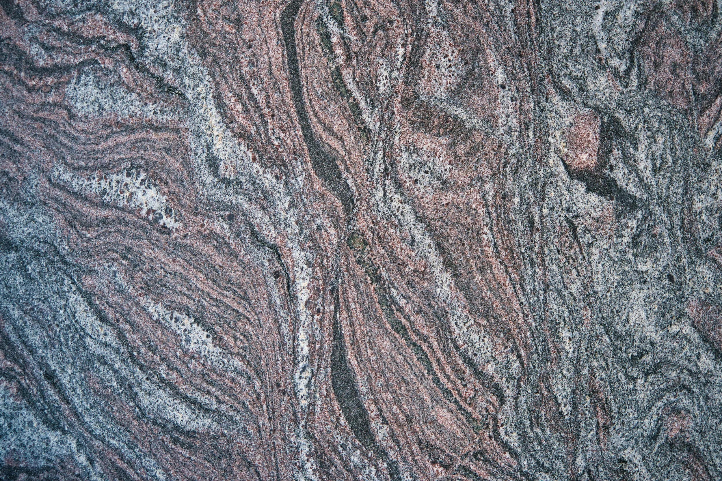 Close-up of a layered, textured rock surface with intricate, swirling patterns in shades of pink, gray, and black.