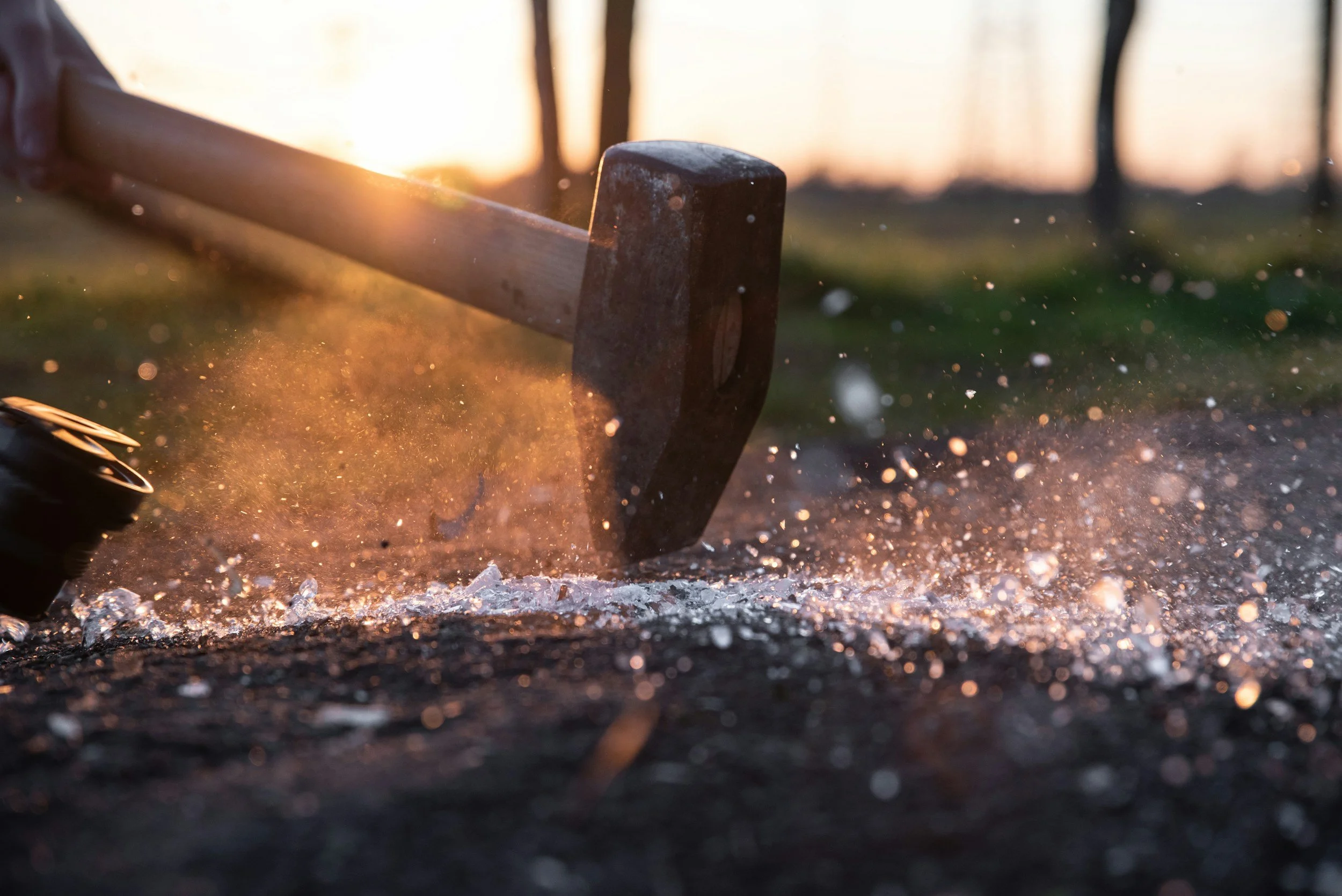 A hammer striking the ground causes dust and debris to scatter on the surface during sunset.