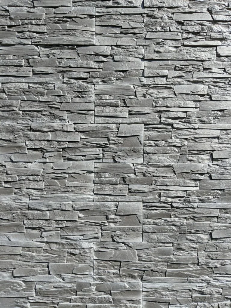 Close-up of a gray stone brick wall with textured, uneven surface and horizontal layout.