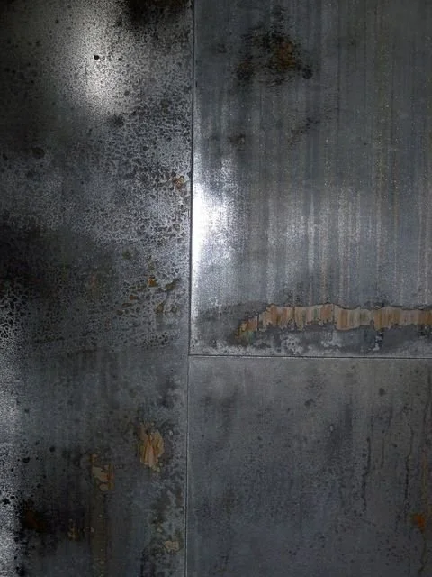 Close-up of a metal surface with rust, stains, and peeling paint.