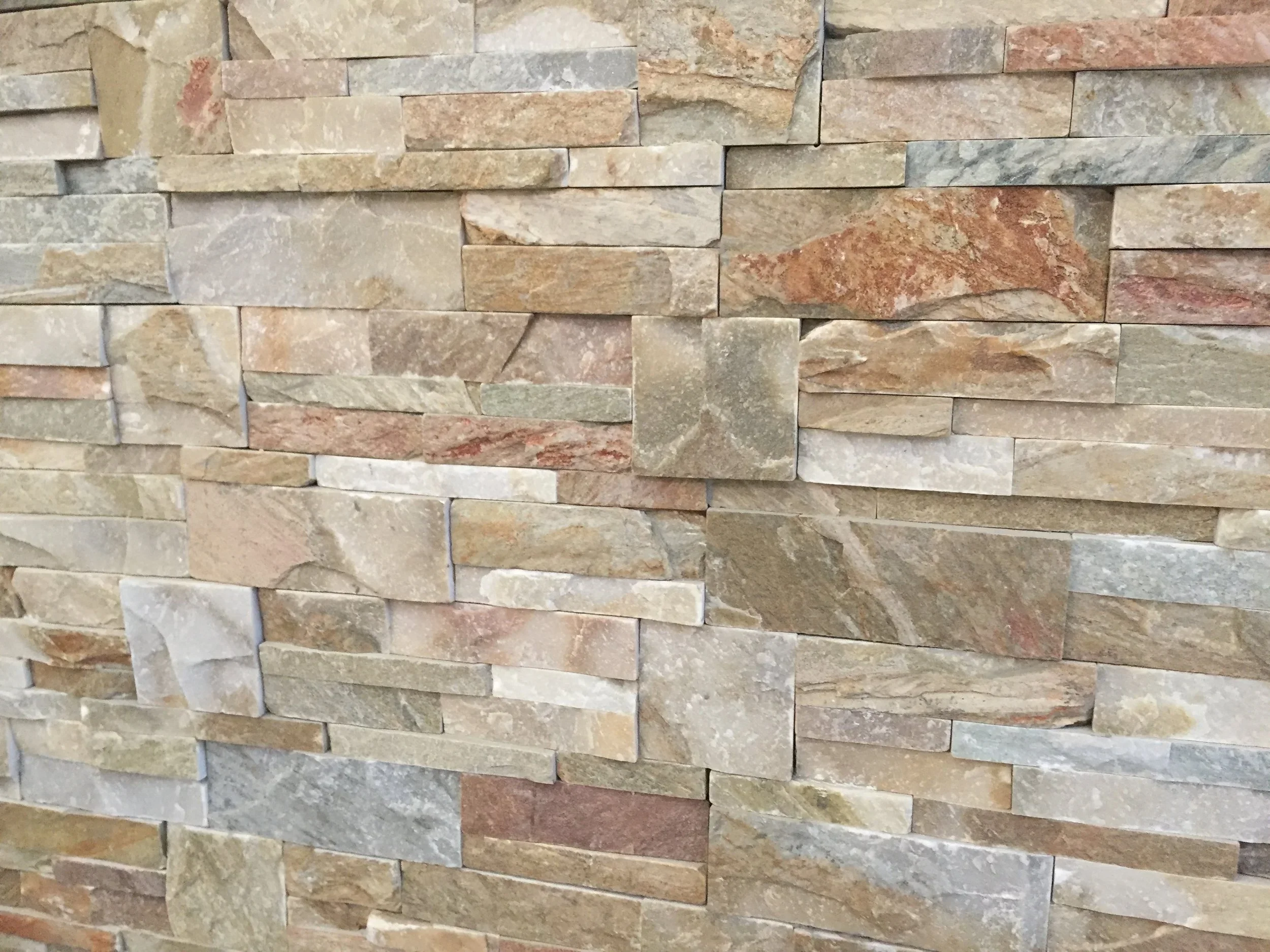Close-up of a wall made of stacked natural stones in various shades of beige, brown, and gray.