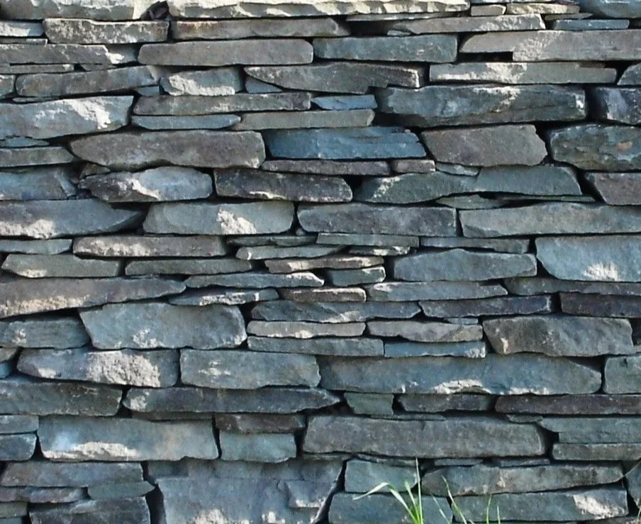Close-up of a dry stone wall built with stacked flat gray rocks.