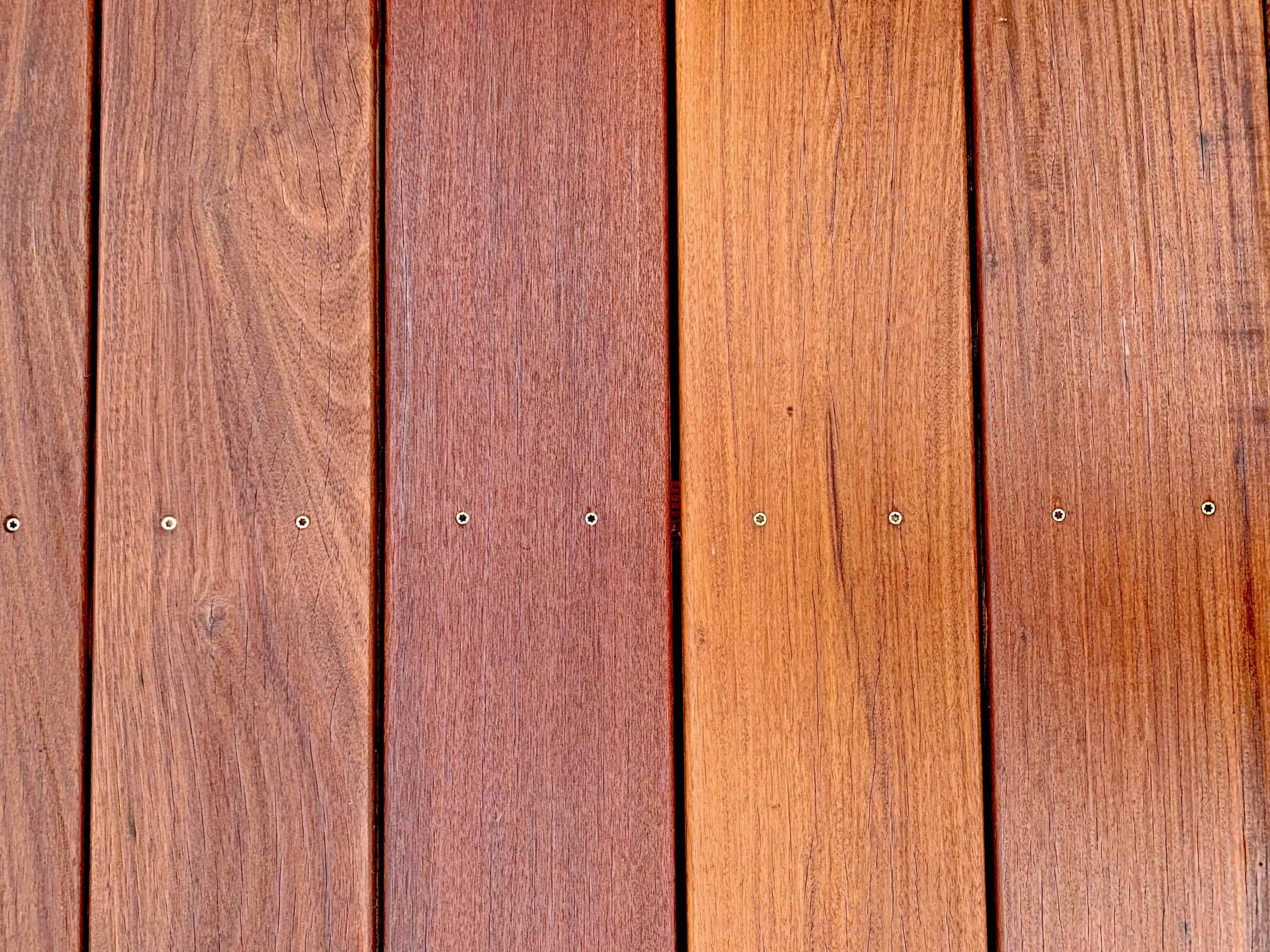 Close-up of a wooden fence with vertical planks in varying shades of brown, secured with small screws.
