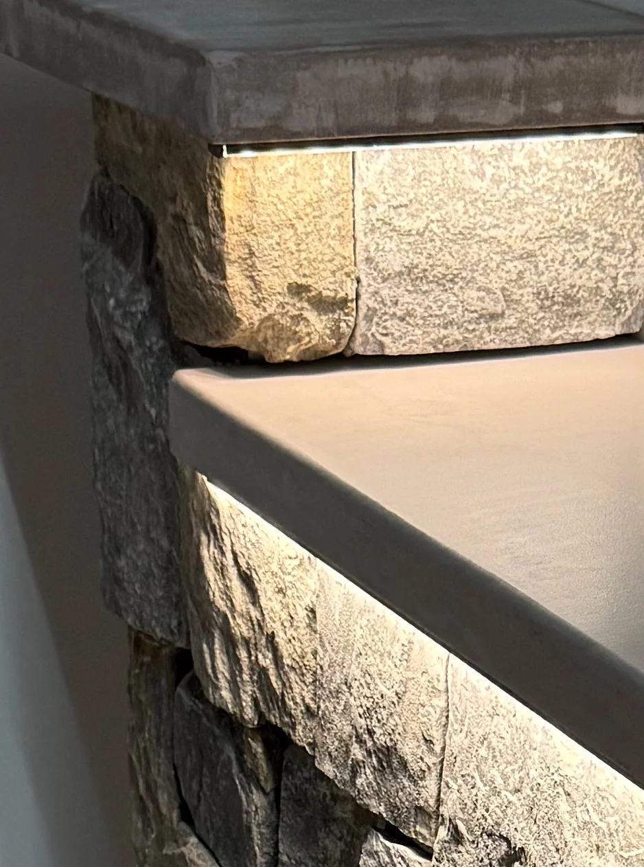 Close-up of a stone fireplace with a wooden mantel and beige stones, partially illuminated by indoor lighting.