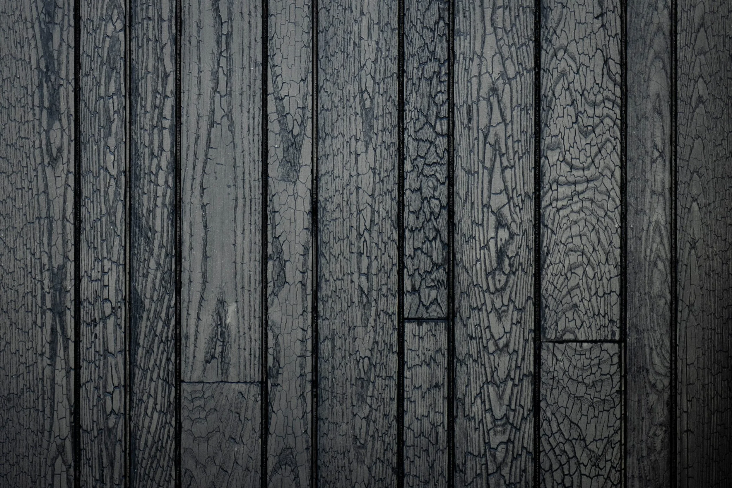 Close-up view of a weathered wooden surface with vertical planks showing cracked and peeling dark gray paint.