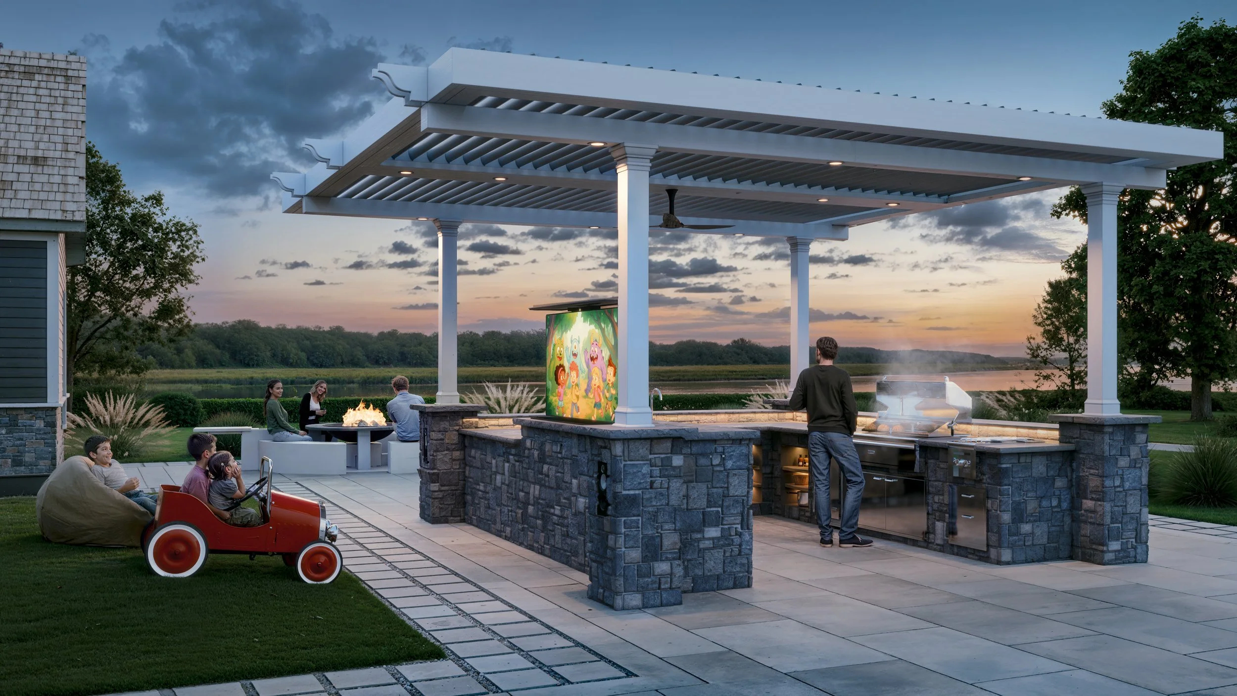 Family enjoying outdoor gathering with fire pit, children in toy car, grilling area, and sunset view near a river.