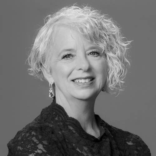 Black and white portrait of a woman with shoulder-length curly hair, smiling, wearing earrings and a lacy top.